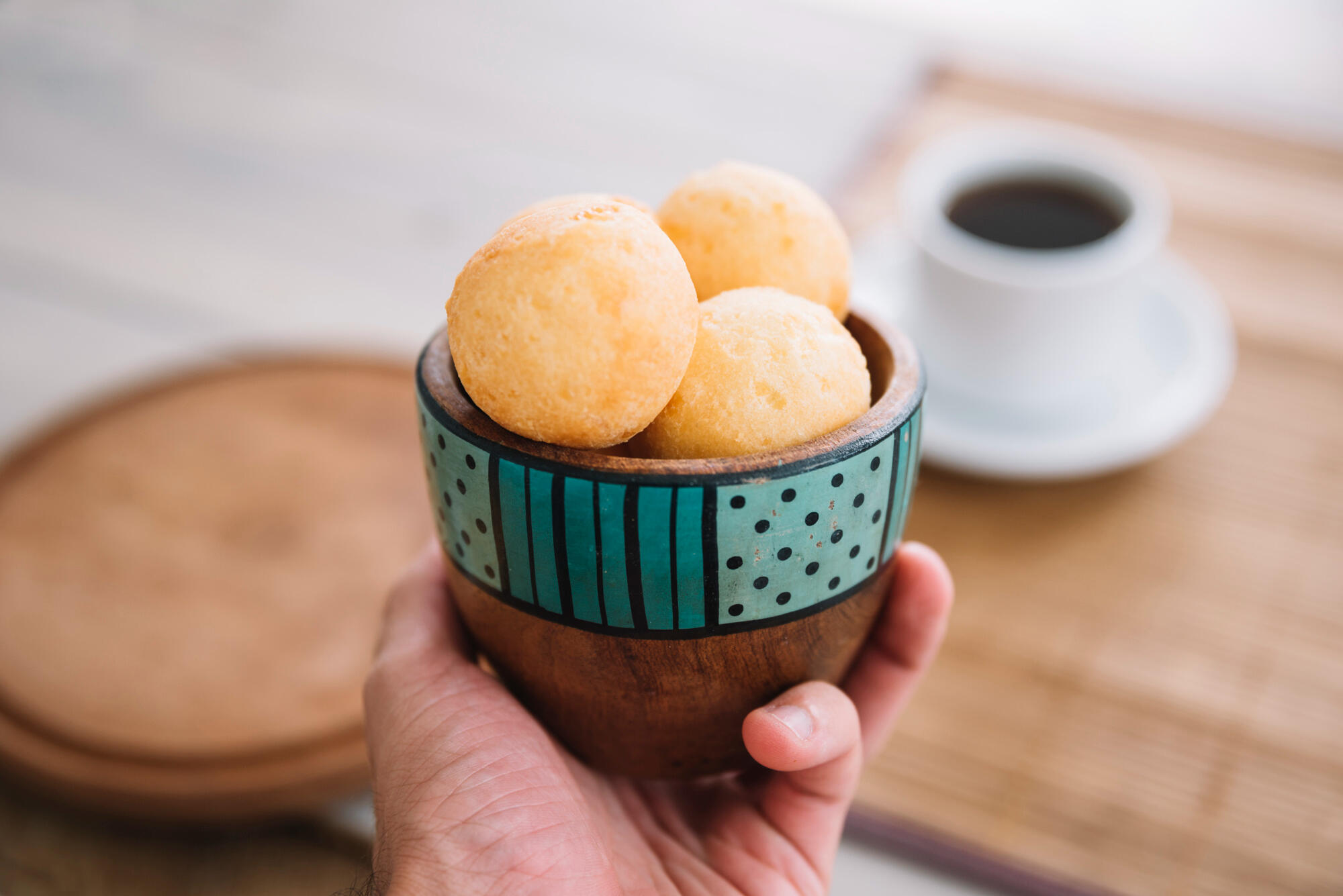 Pão de queijo na cesta e café na xícara, em cima da mesa.
