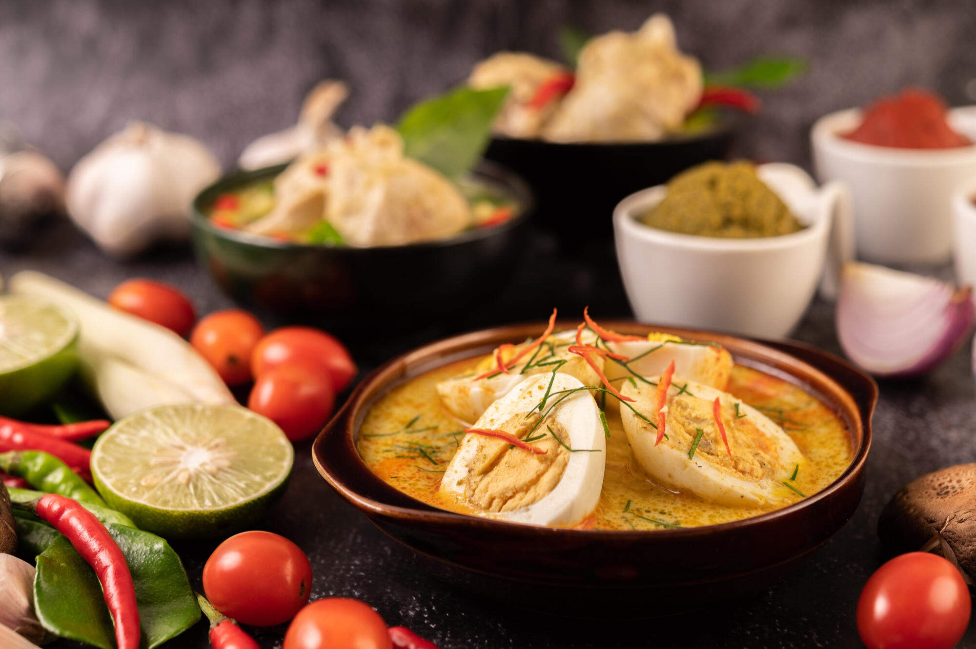 Moqueca dentro da cuia e legumes e temperos em cima da mesa.