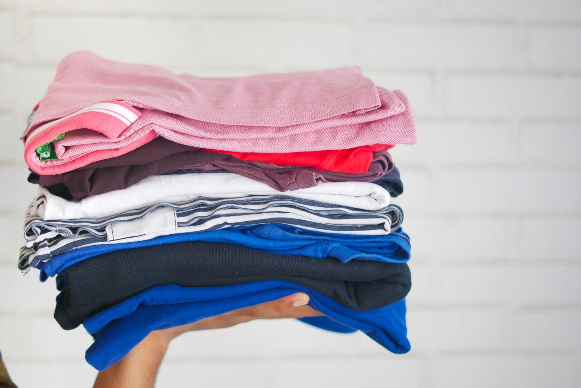 Mão segurando uma pilha de roupas dobradas.