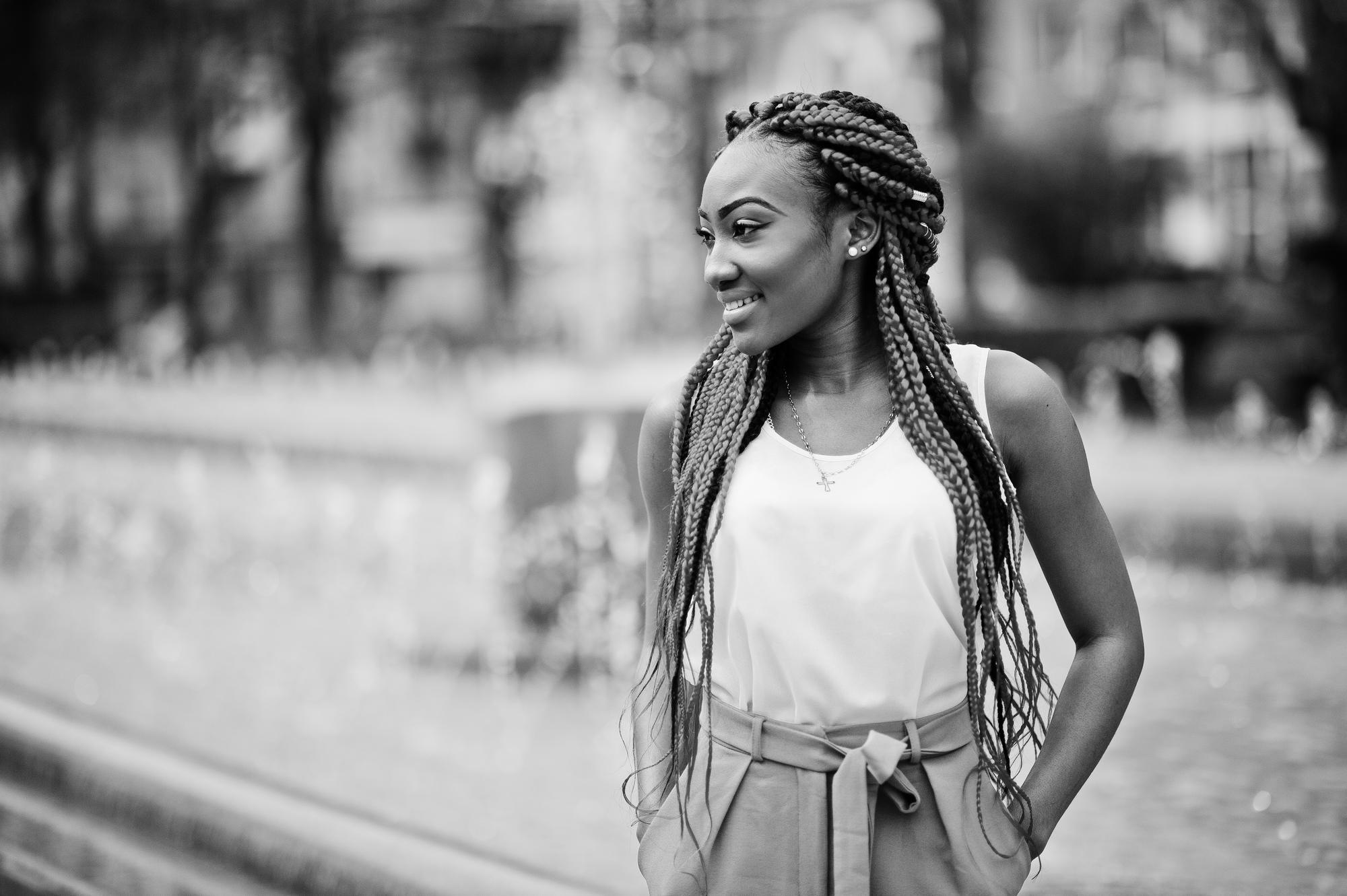 Mulher em pé, com a mãos no bolso e olhando para o lado, usando tranças box braids.