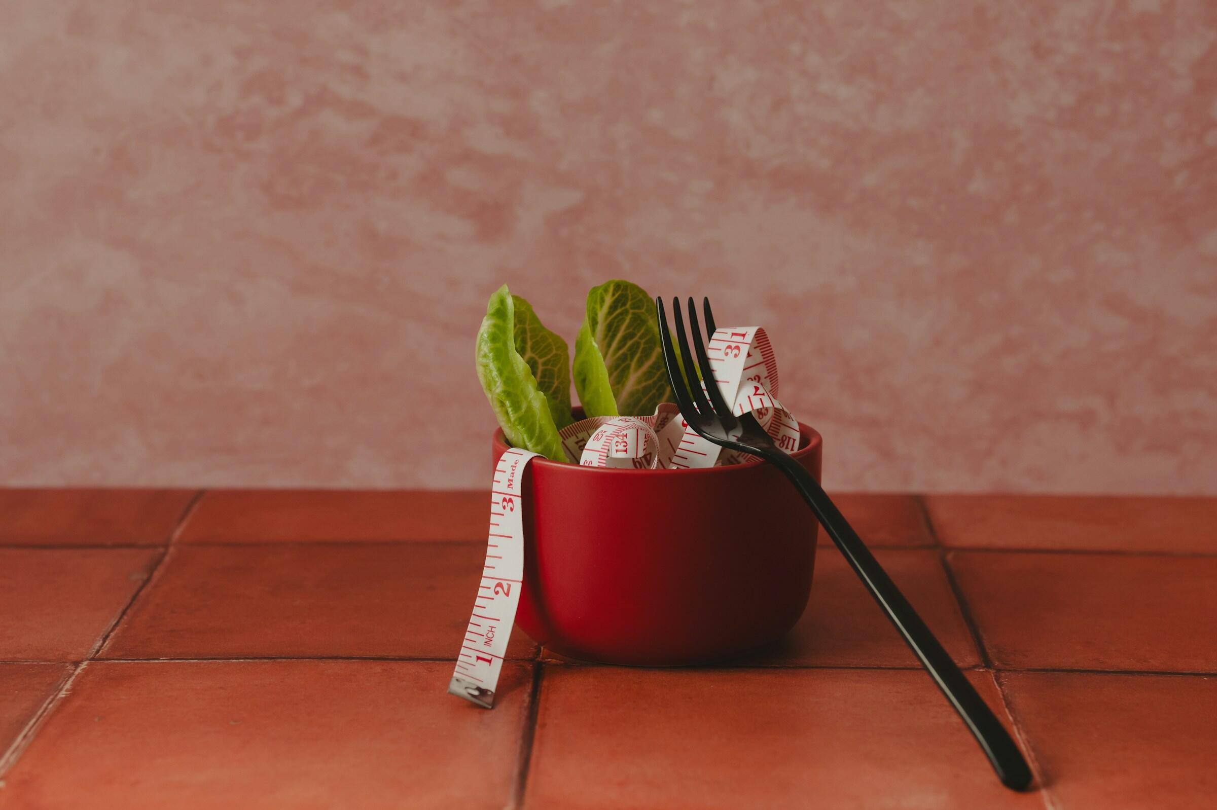 Tijela com salada e uma fita métrica dentro e um garfo apoiado
