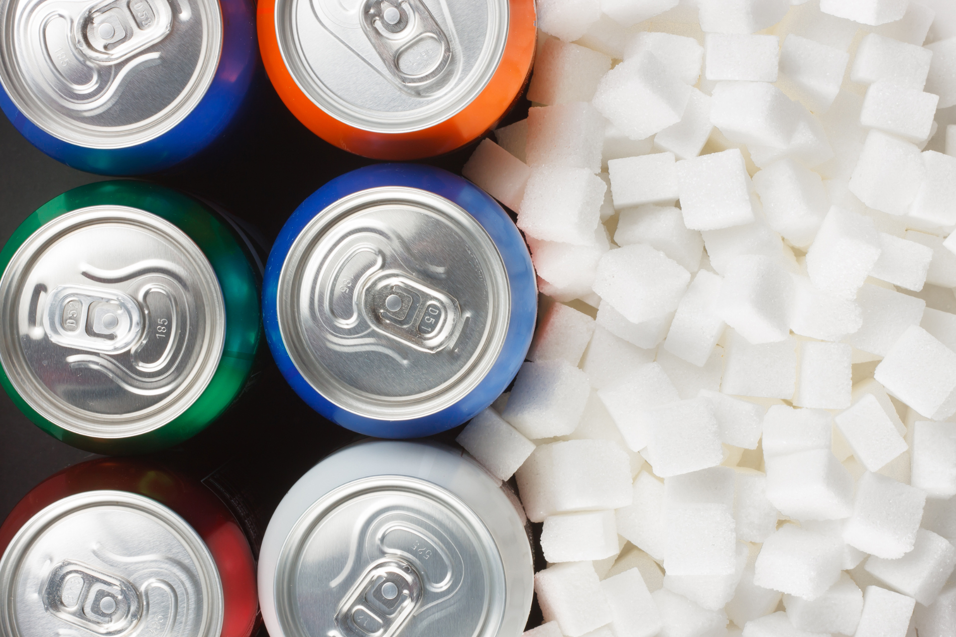 Latas de refrigerante alinhadas com uma quantidade generosa de cubos de açúcar ao lado.