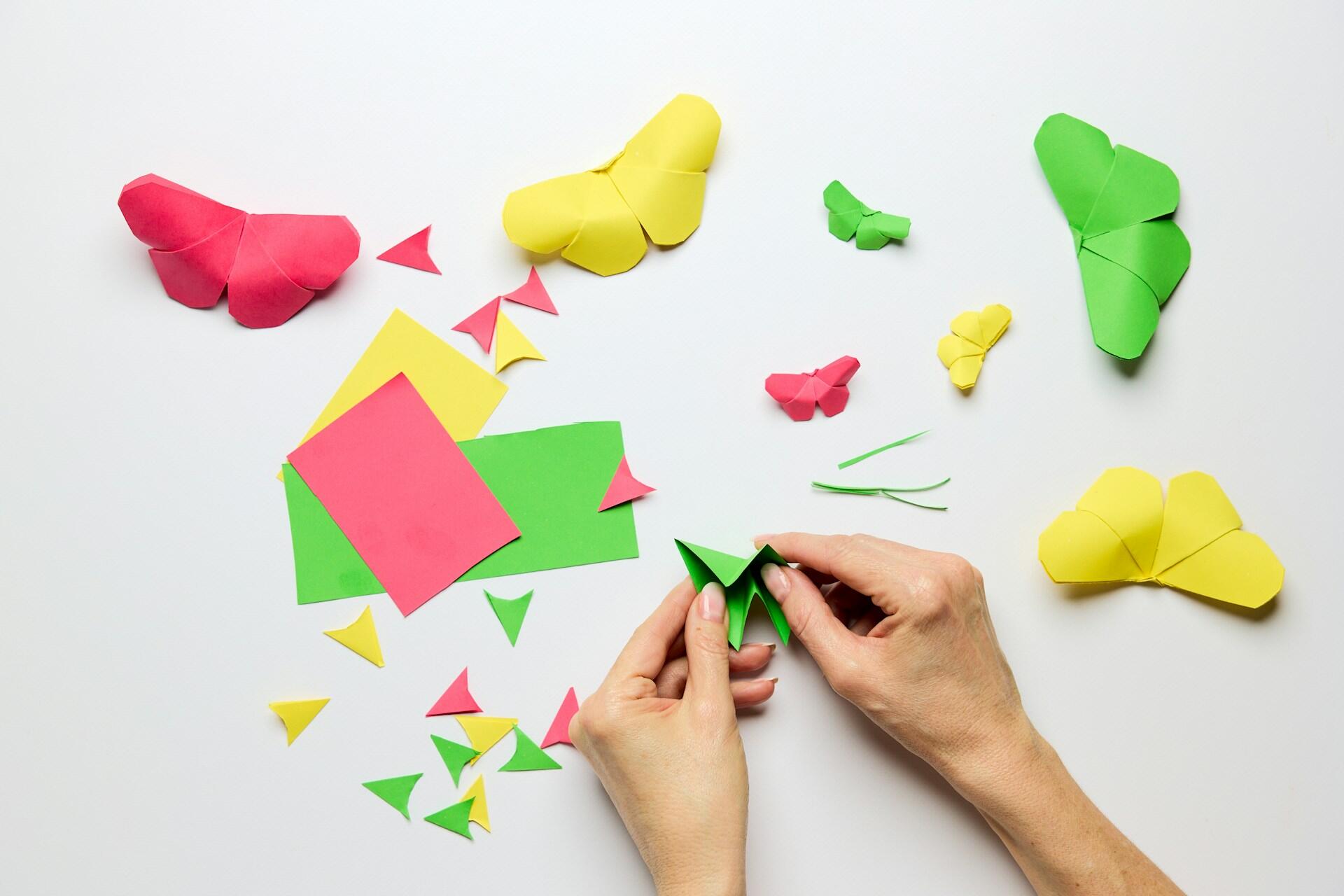 Mãos sobre uma mesa fazendo origamis em forma de borboleta