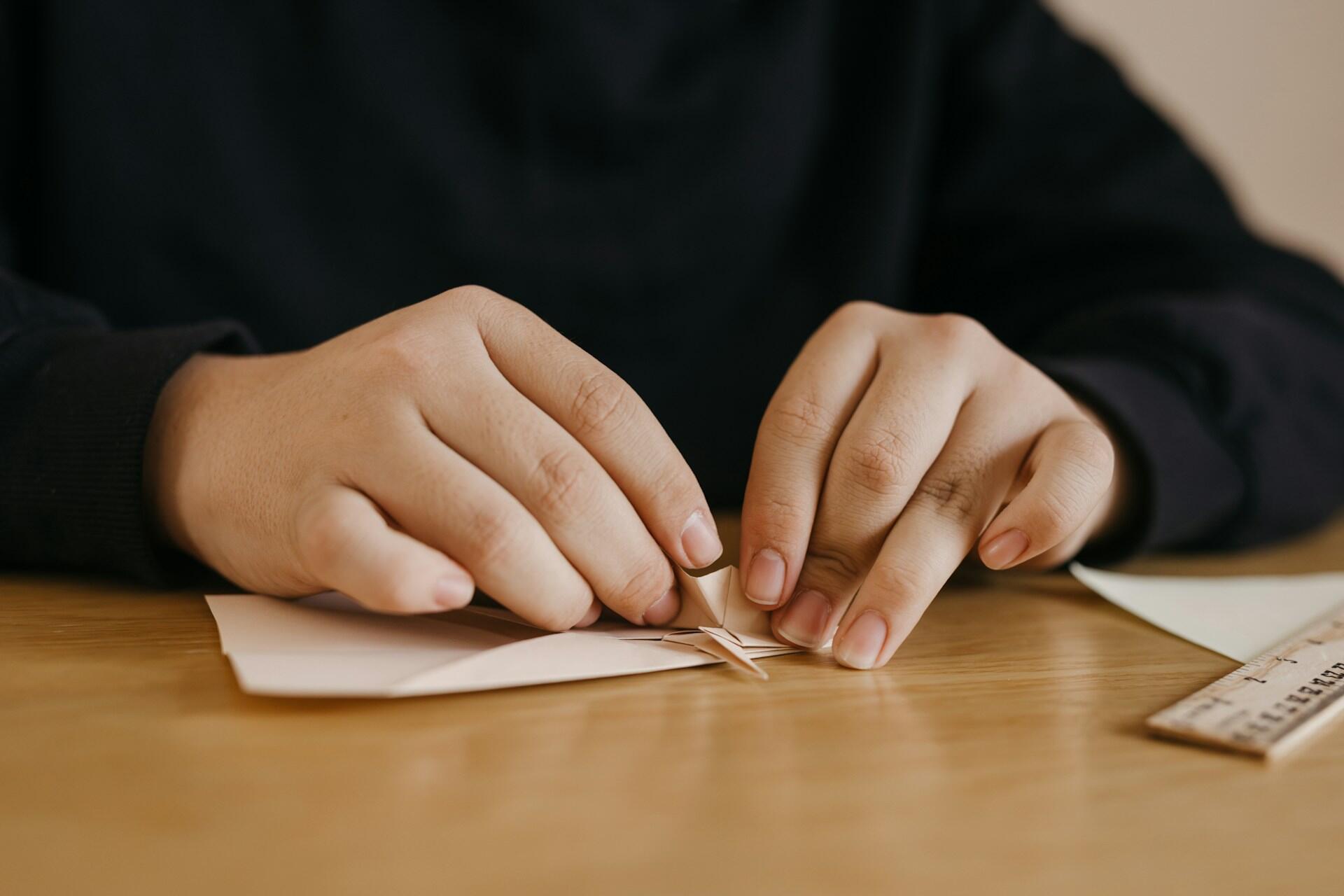 Mãos dobrando um origami sob uma mesa