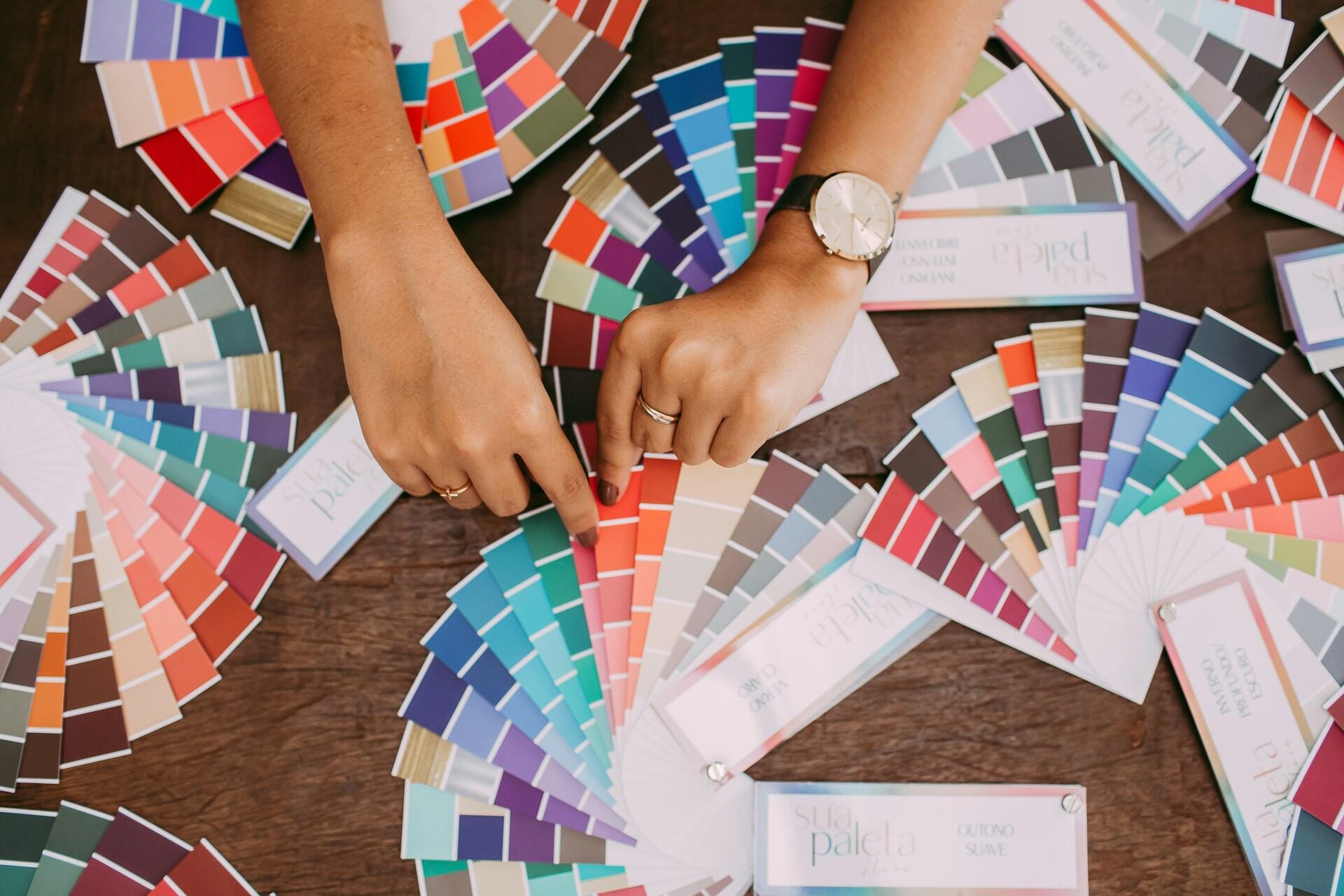 Mãos em uma mesa com várias paletas de cores expostas