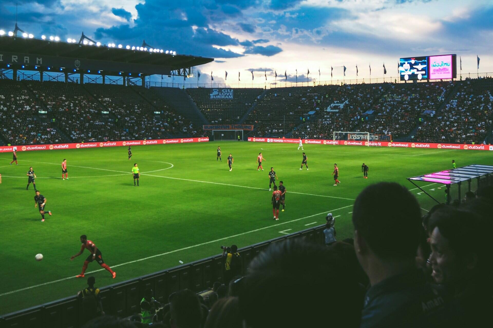 Estádio de futebol, com jogo decorrendo.
