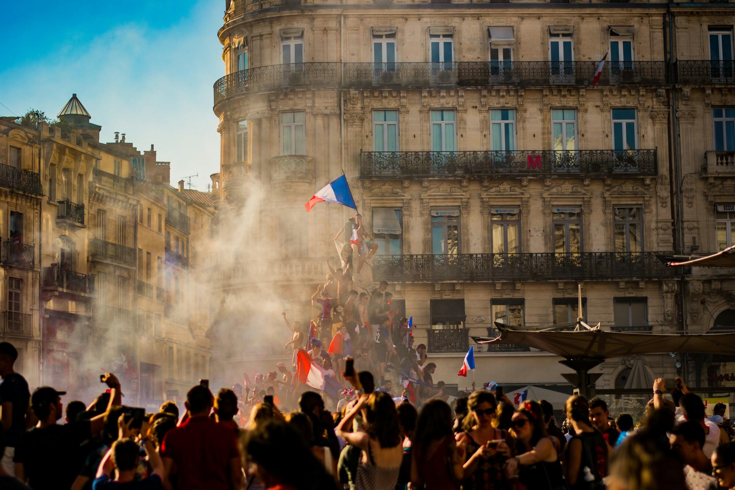 População francesa em multidão, com algumas pessoas segurando a bandeira da França.
