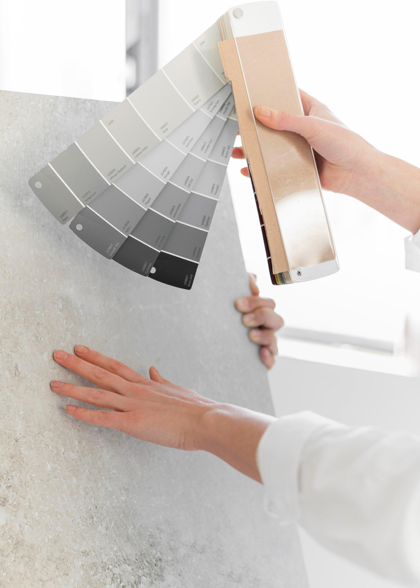 Pessoa com imagens de cores neutras na mão e outra pessoa comparando as cores com a cor de uma pedra. 