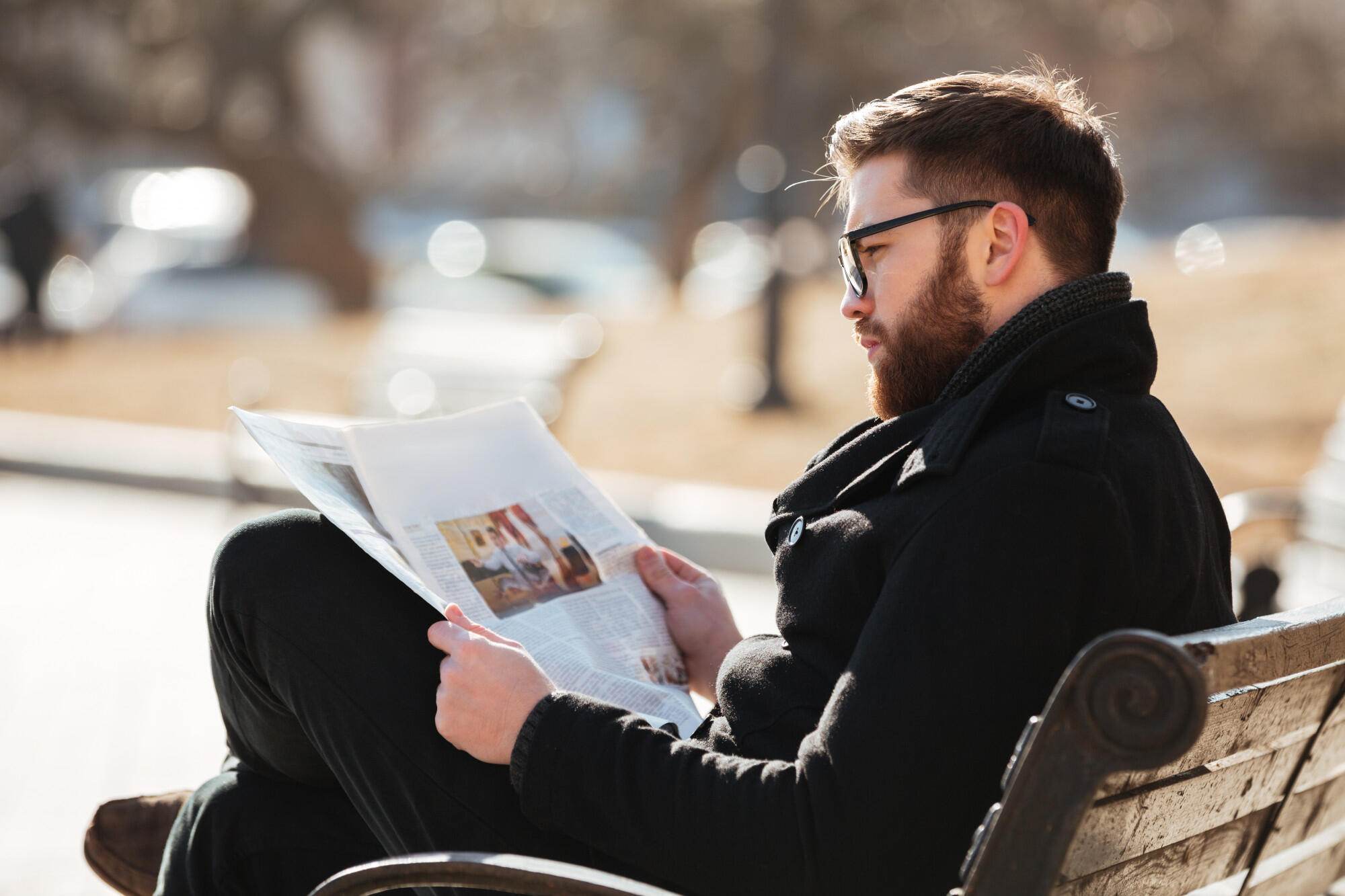 Pessoa lendo o jornal no banco da praça.