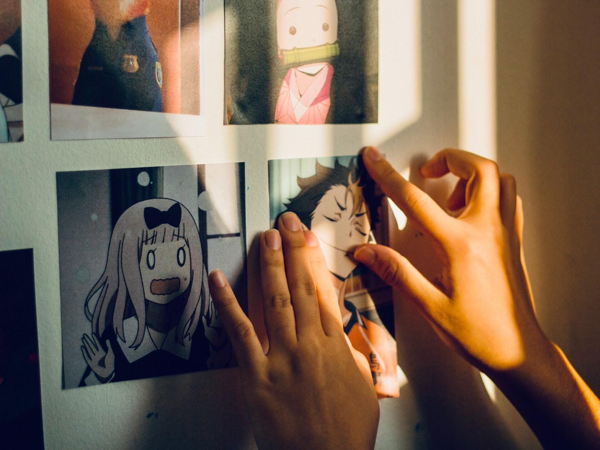 Pessoa tocando fotografias de personagens de anime em uma parede.