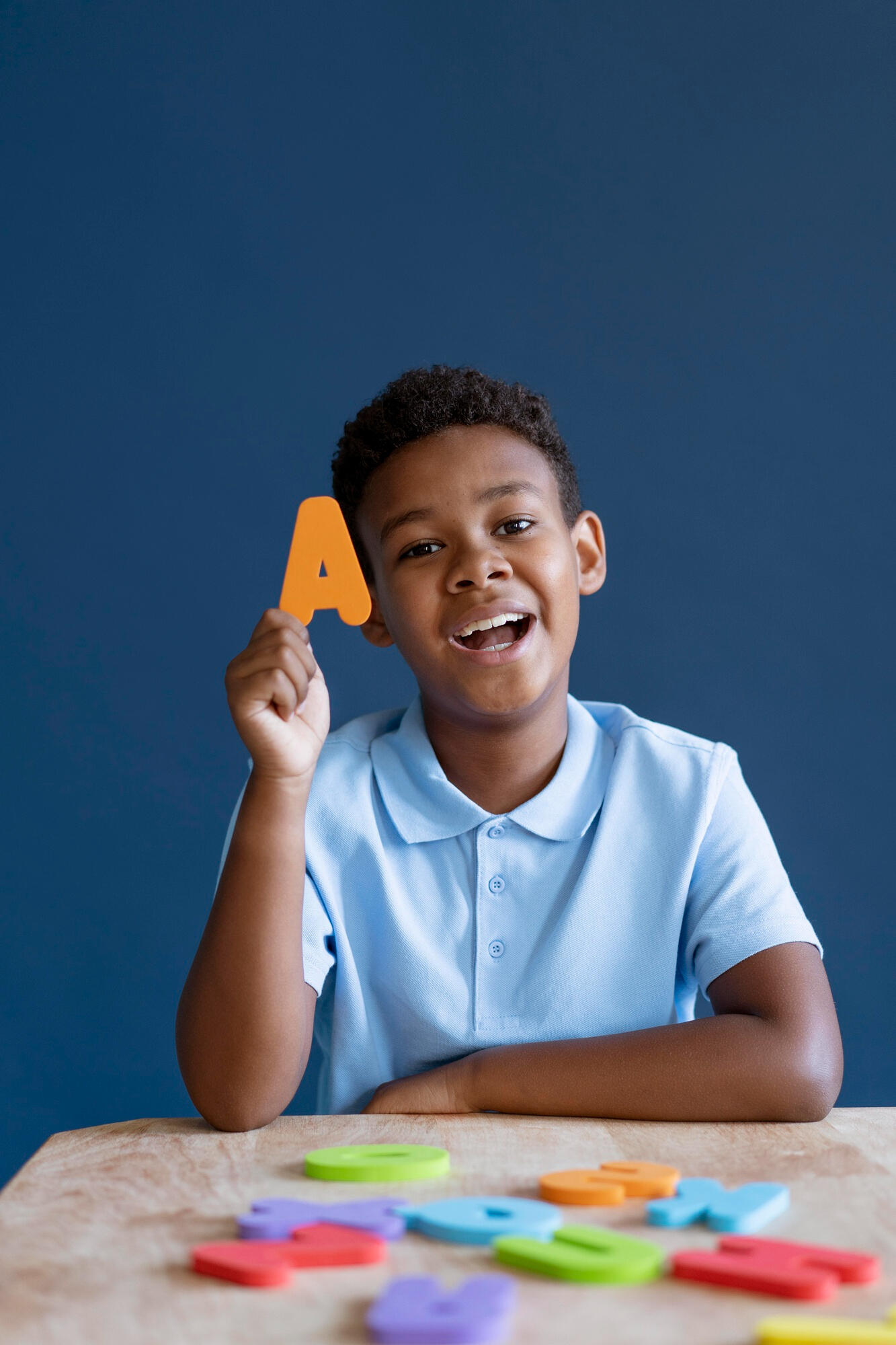 Menino falando as letras do alfabeto e segurando a letra A.