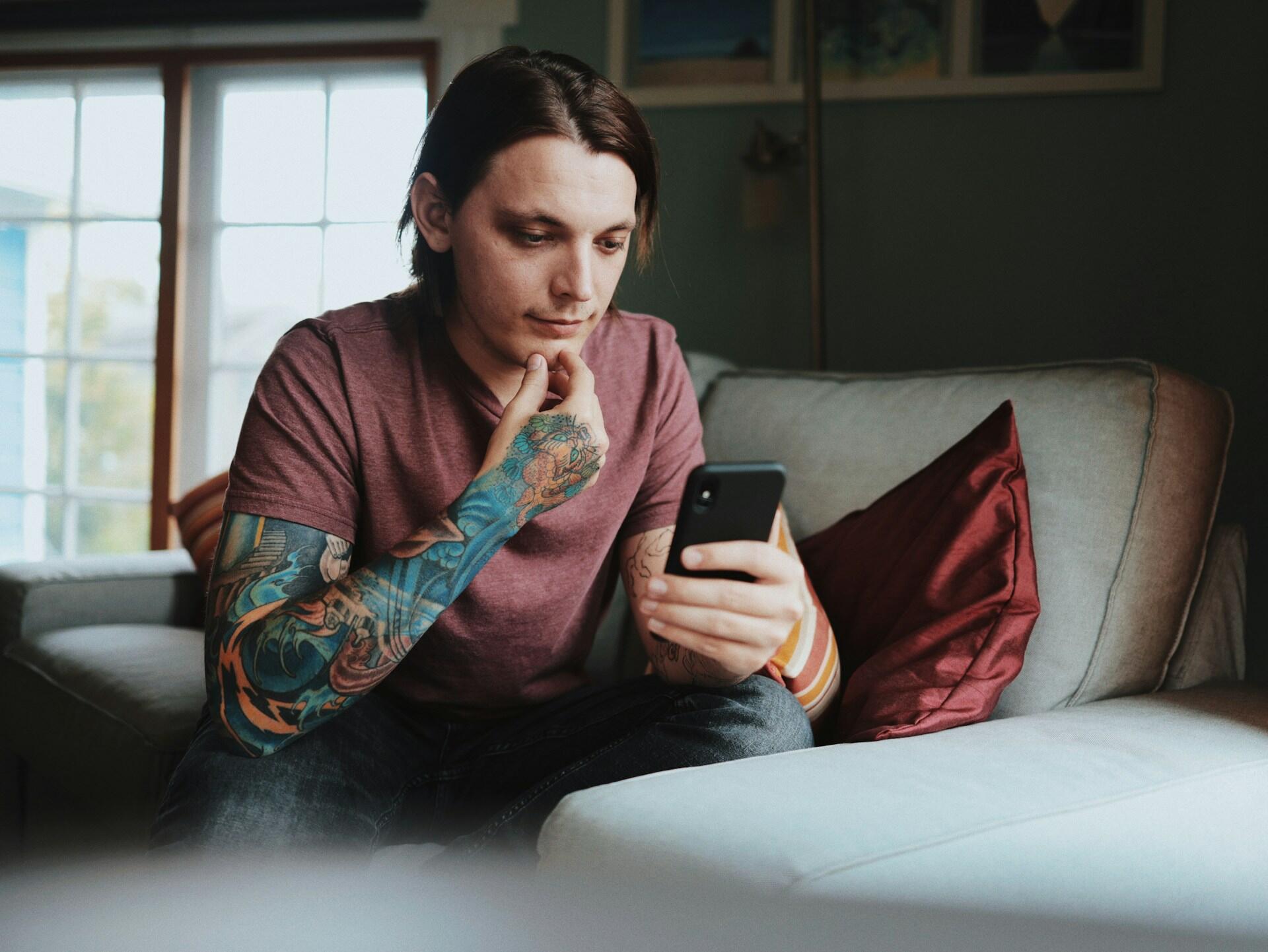 Homem tatuado vendo seu celular