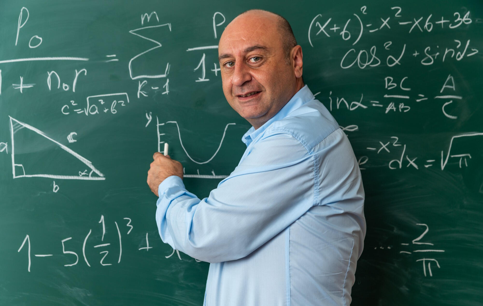 Professor de matemática explicando a matéria e escrevendo na lousa.