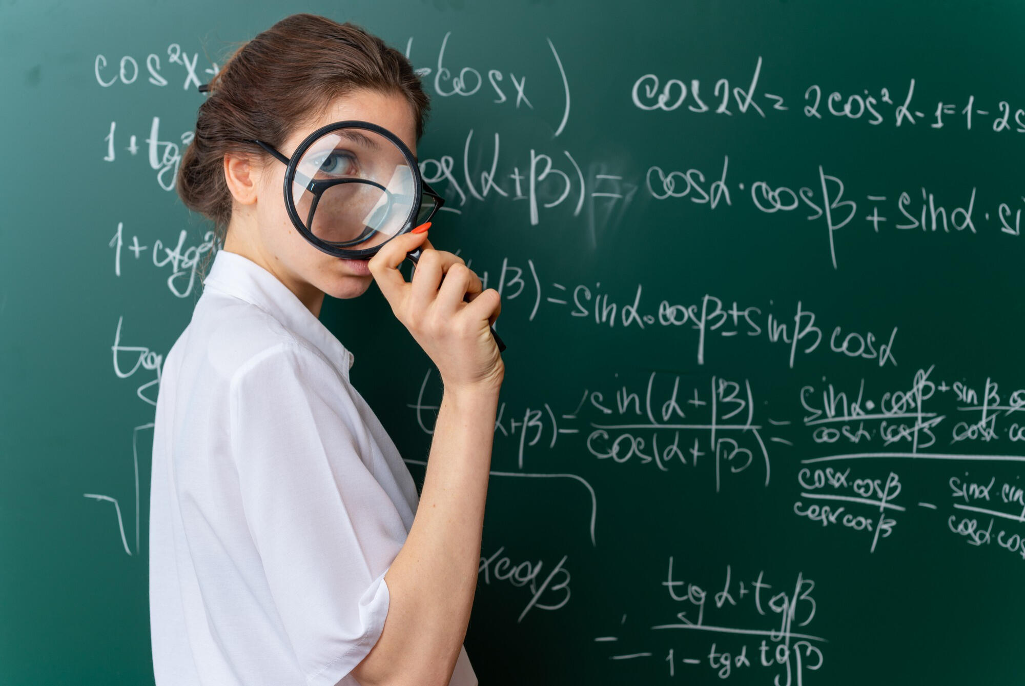 Aluna com uma lupa resolvendo exercícios de matemática na lousa.