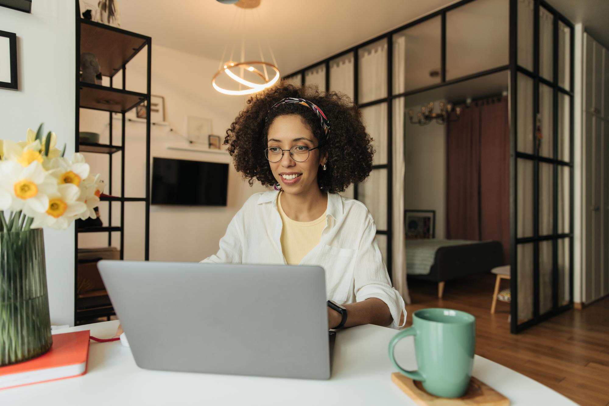 Mulher trabalhando em casa, com notebook e xícara de café ao lado.