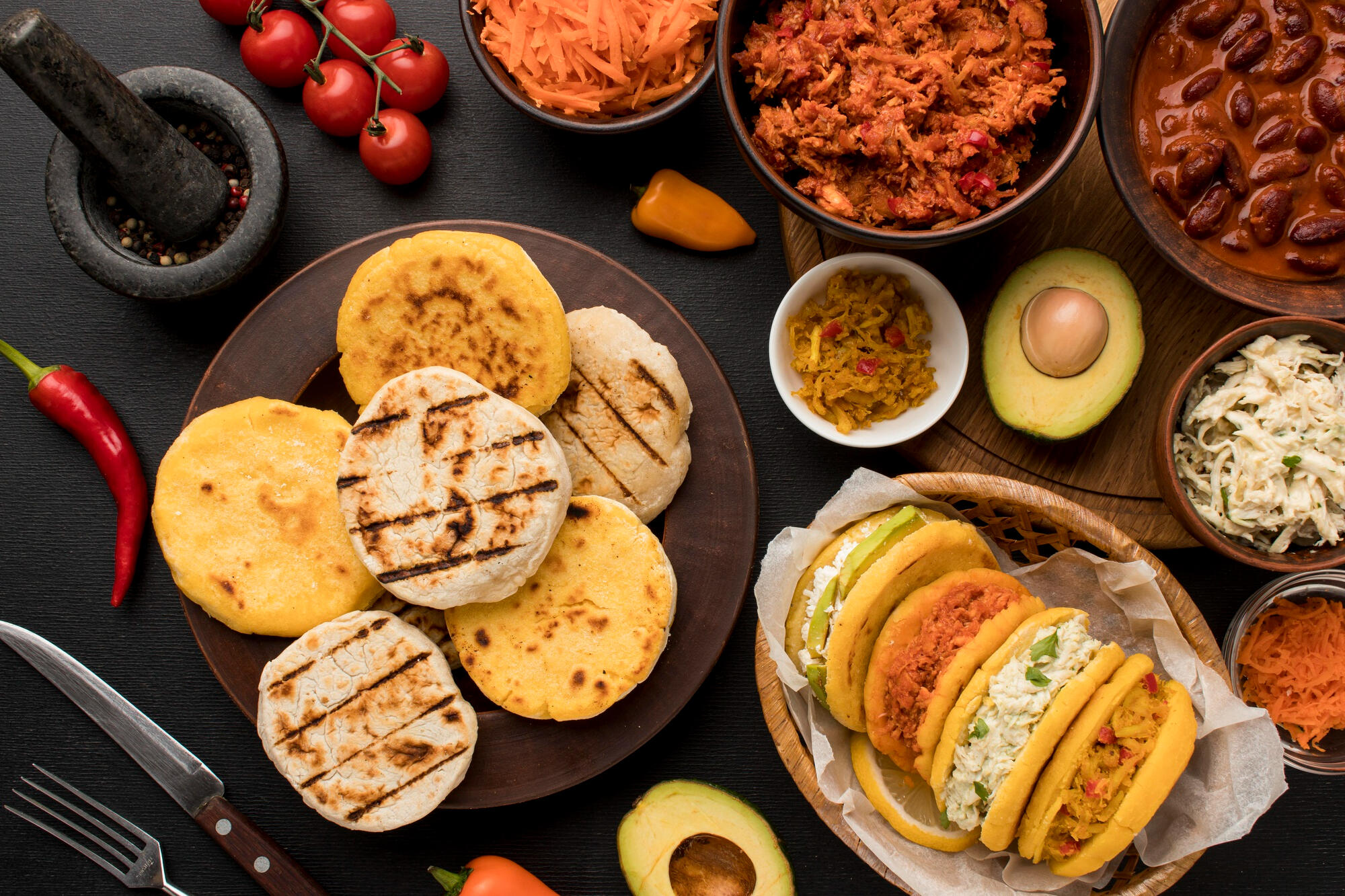 Arepa, abacate, carne desfiada e outros ingredientes da culinária venezuelana em cima da mesa.