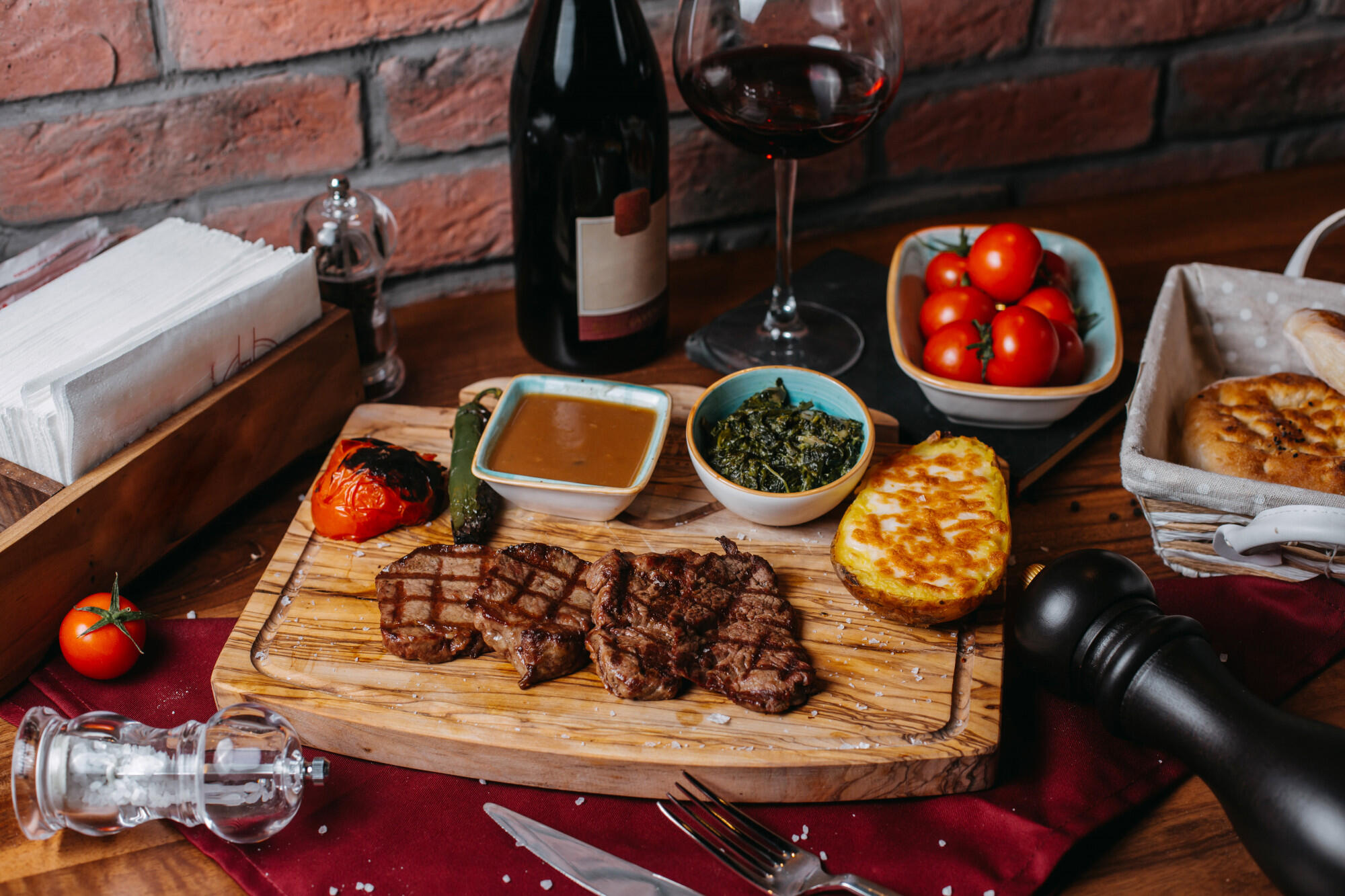 Carne na tábua, com temperos em cima da mesa e garrafas de vinho.