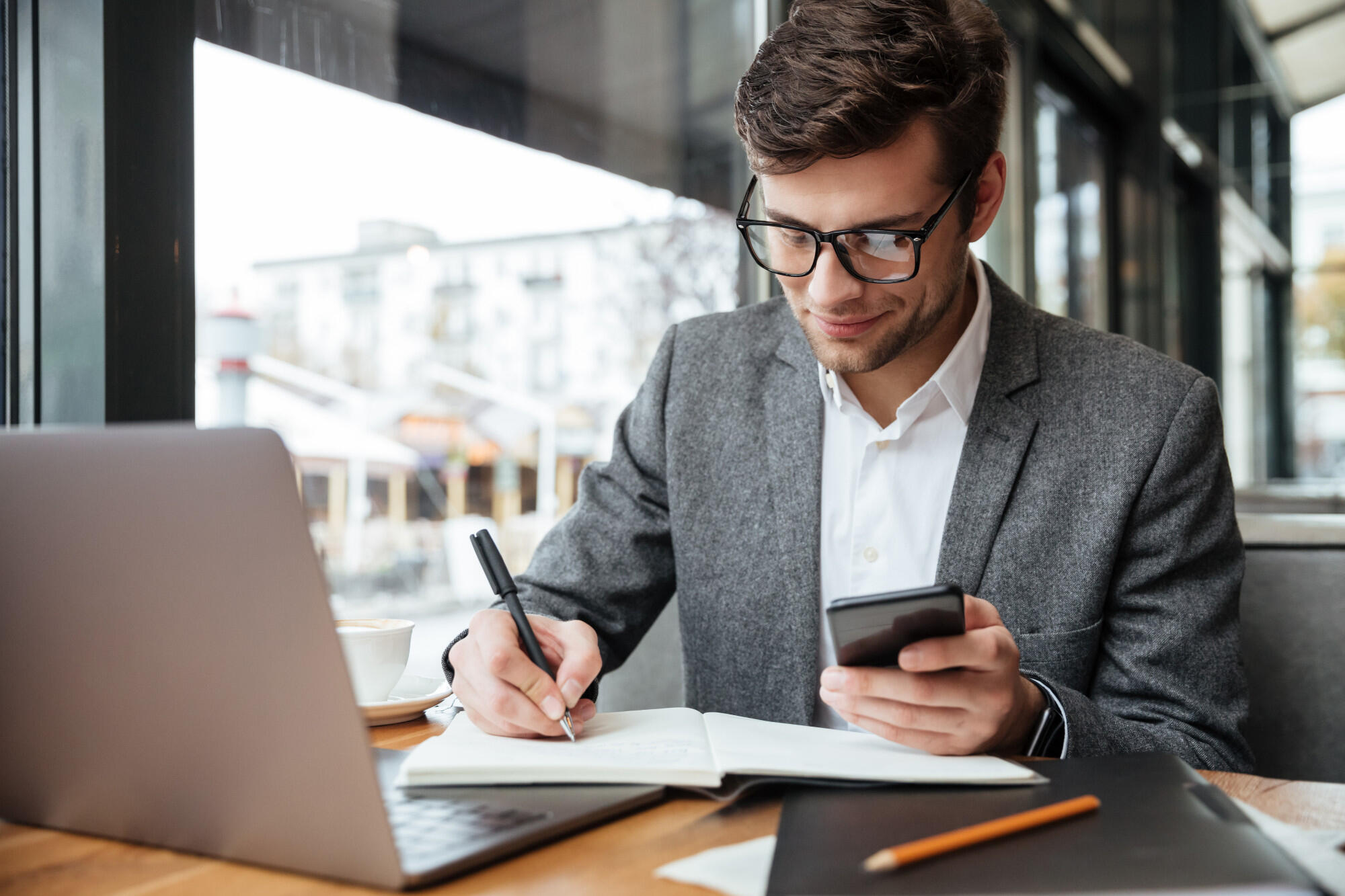 Assistente financeiro trabalhando, escrevendo com uma mão e o celular na outra mão.