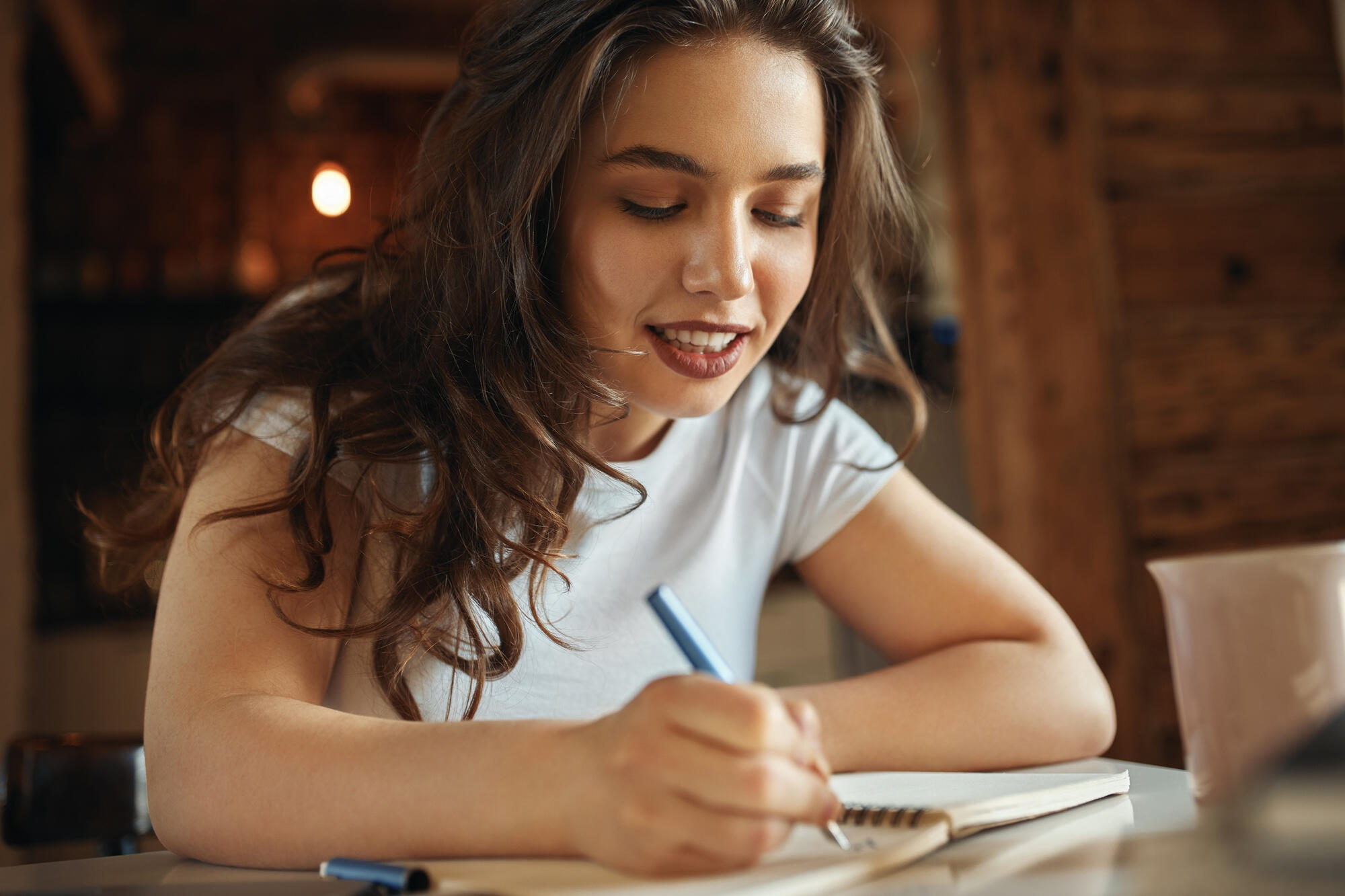 Menina escrevendo texto dissertativo argumentativo no caderno, usando lápis.