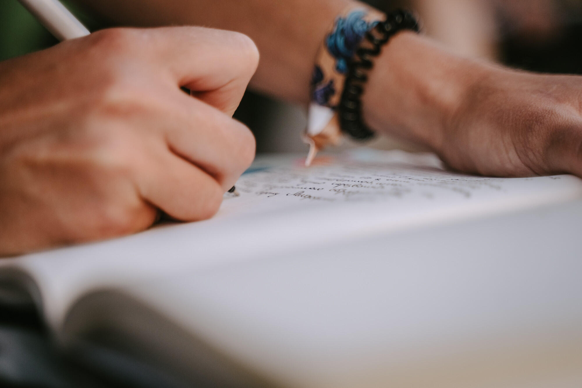 Mão de pessoa escrevendo texto injuntivo no caderno com lápis.