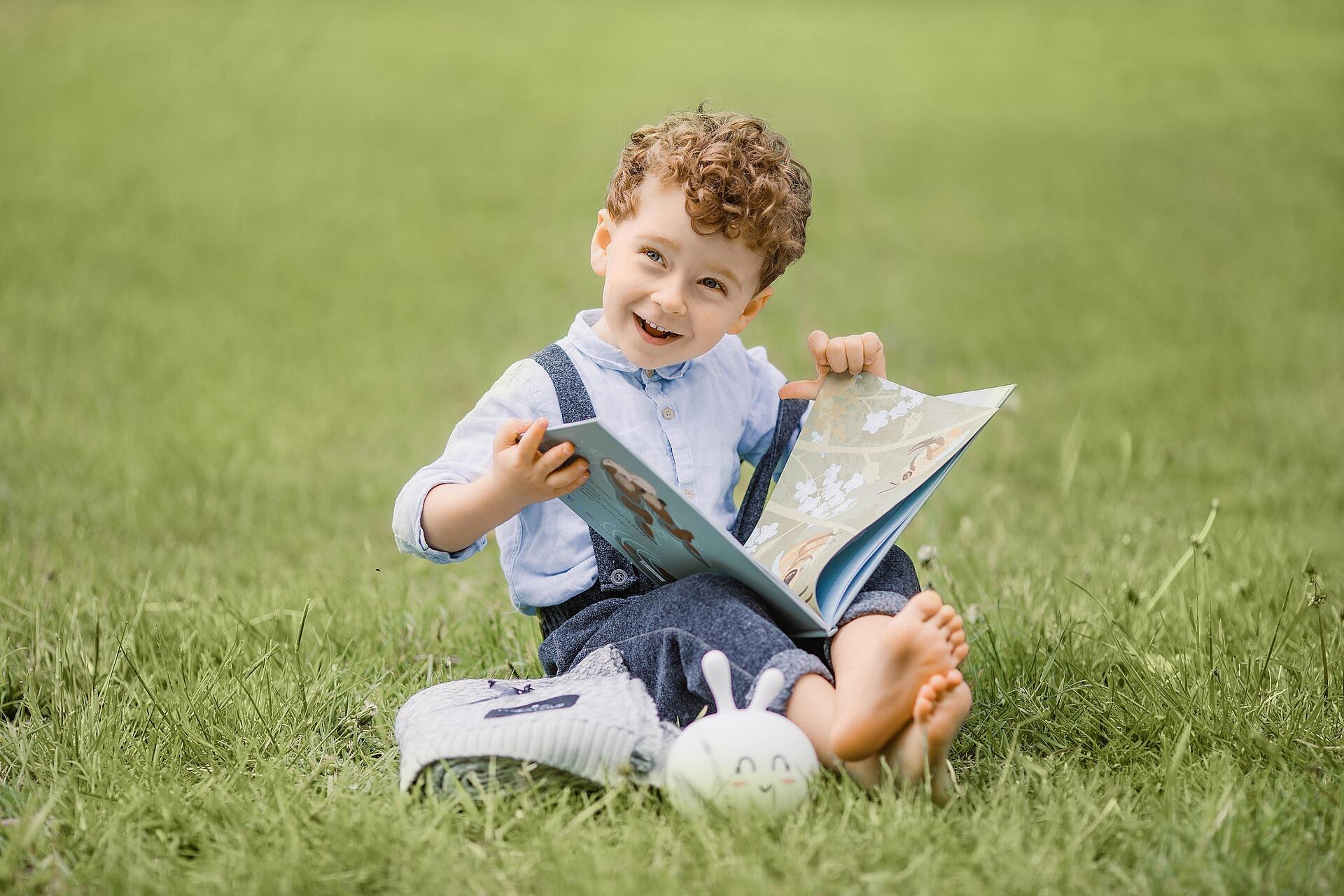 Imagem de um menino lendo livro em um gramado