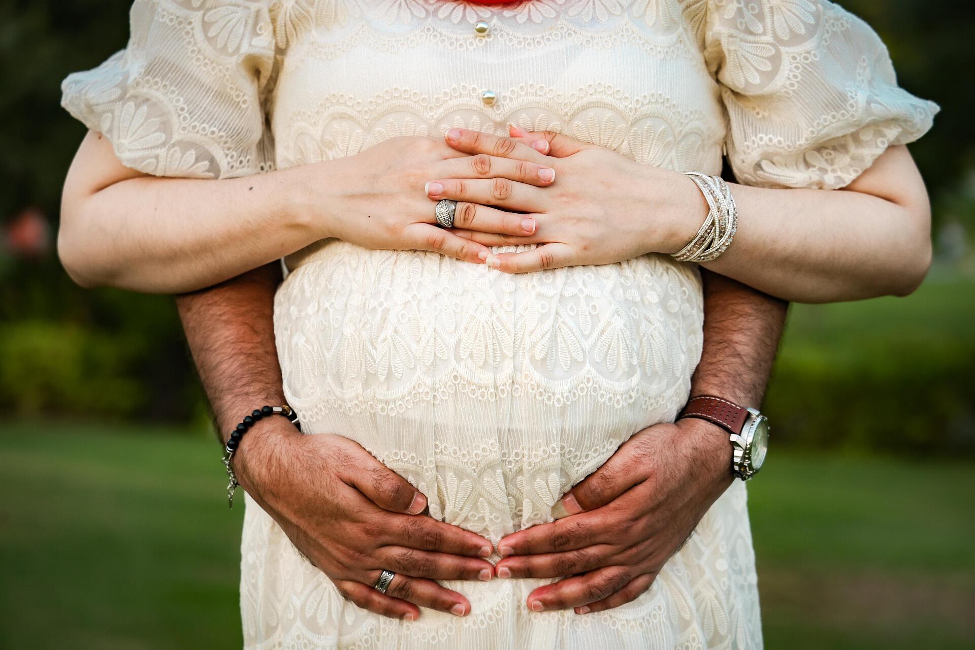 mulher e homem abraçando uma barriga gestante.