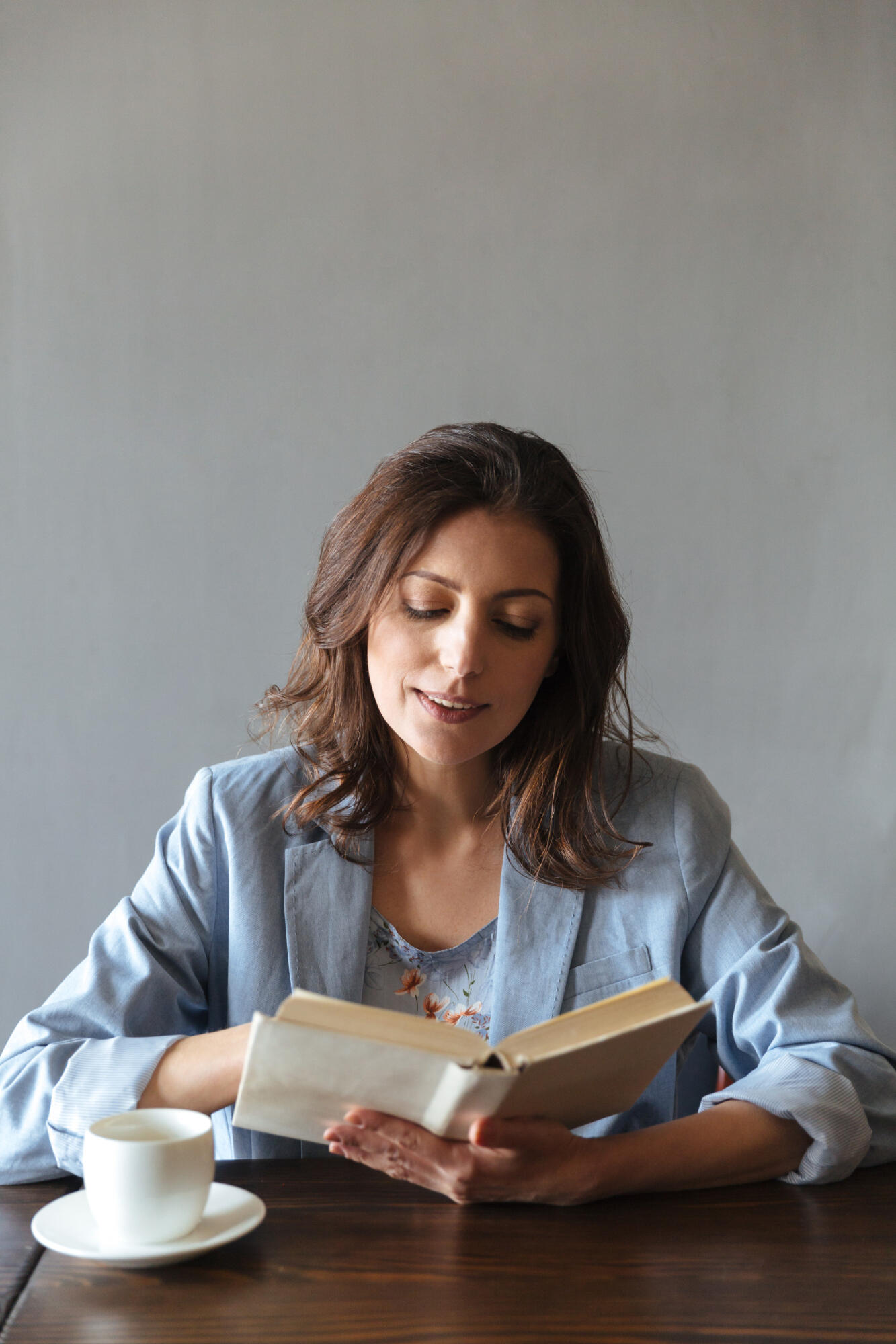 Mulher lendo livro sentada com café sob a mesa.