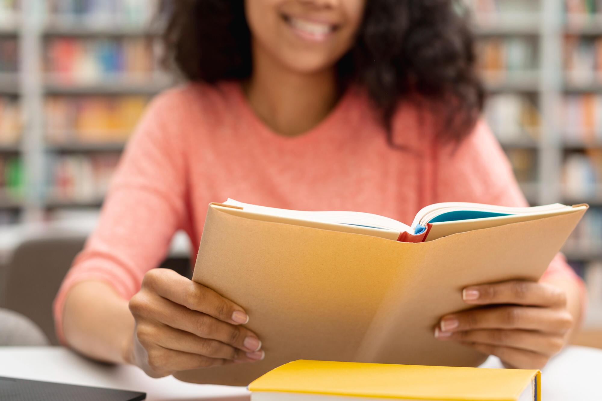 Mulher lendo livro aberto e sorrindo sentada na biblioteca.