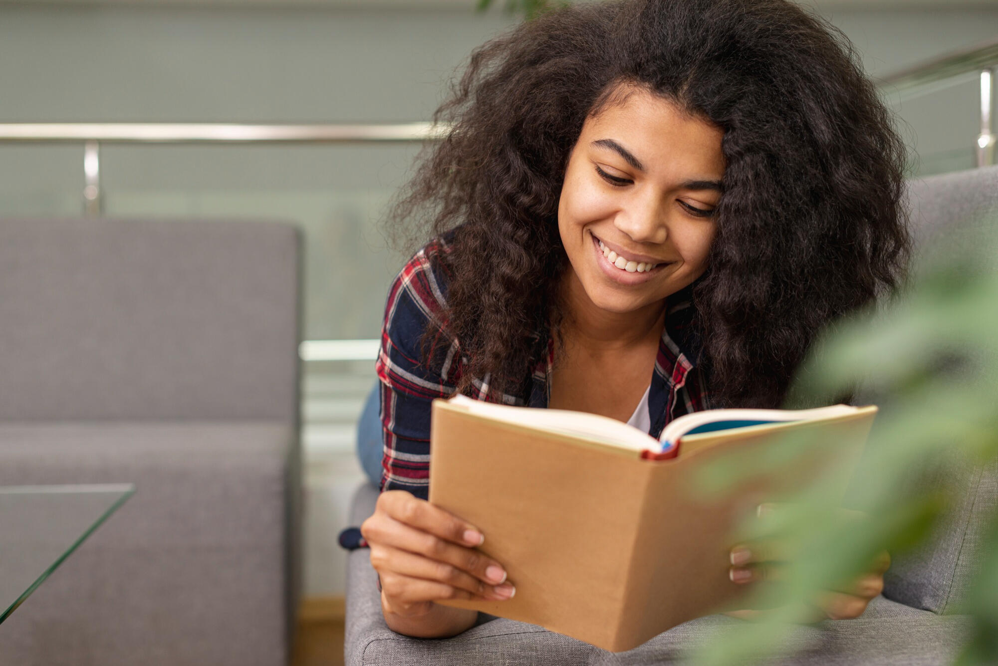 Mulher lendo livro, deitada de bruços e sorridente.