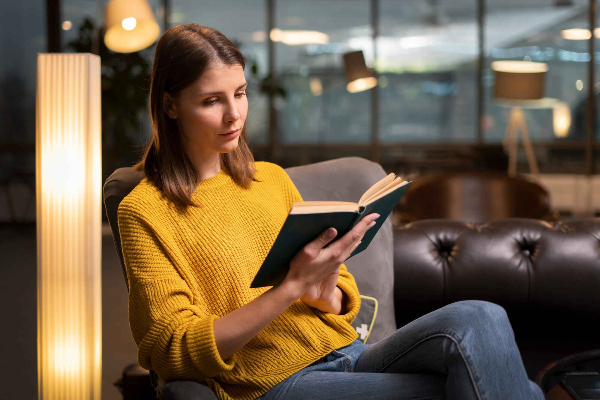 Mulher lendo livro sentada na poltrona.