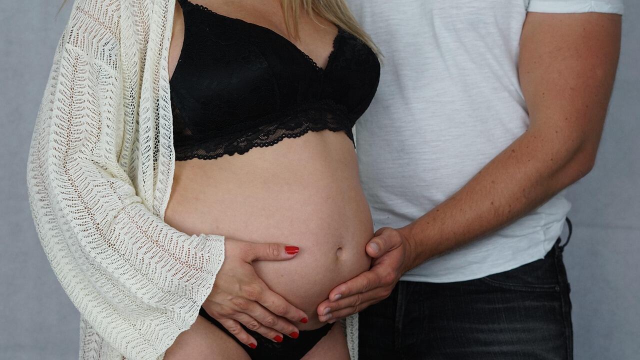 Mulher grávida ao lado de um homem, ambos com a mão na barriga