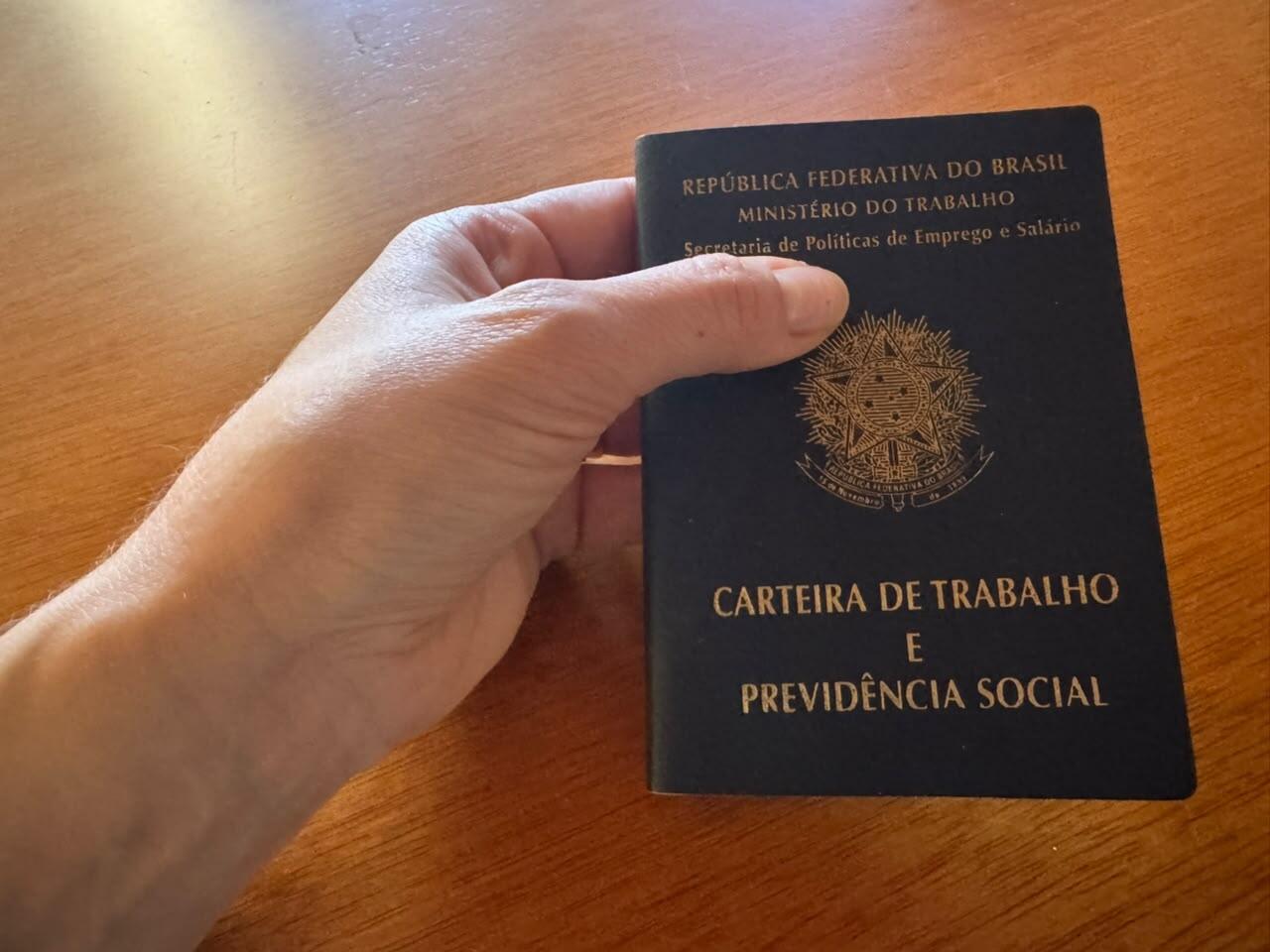 Imagem de uma mão segurando uma carteira de trabalho.