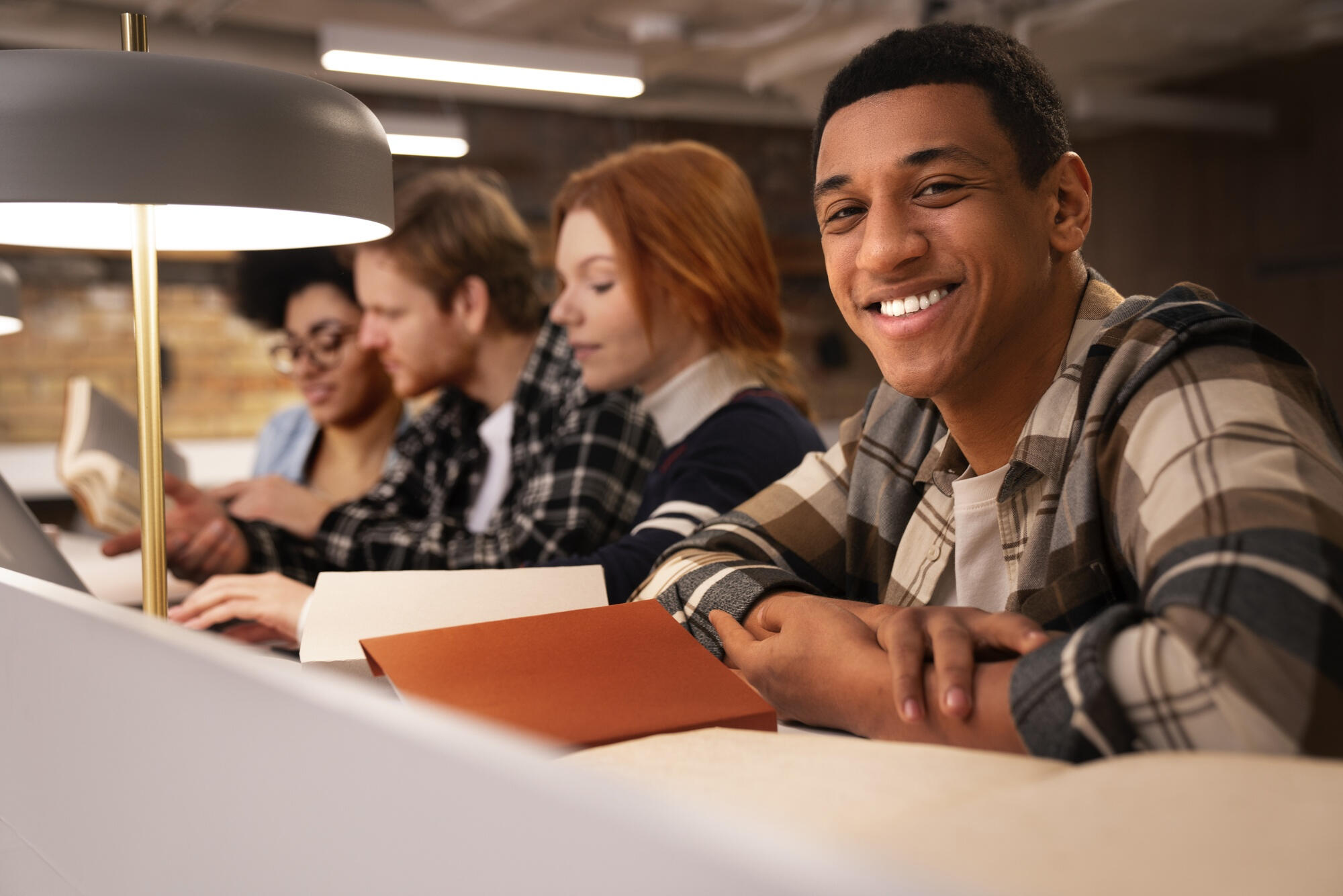 Alunos estudando em bilbioteca, com livro na mão.