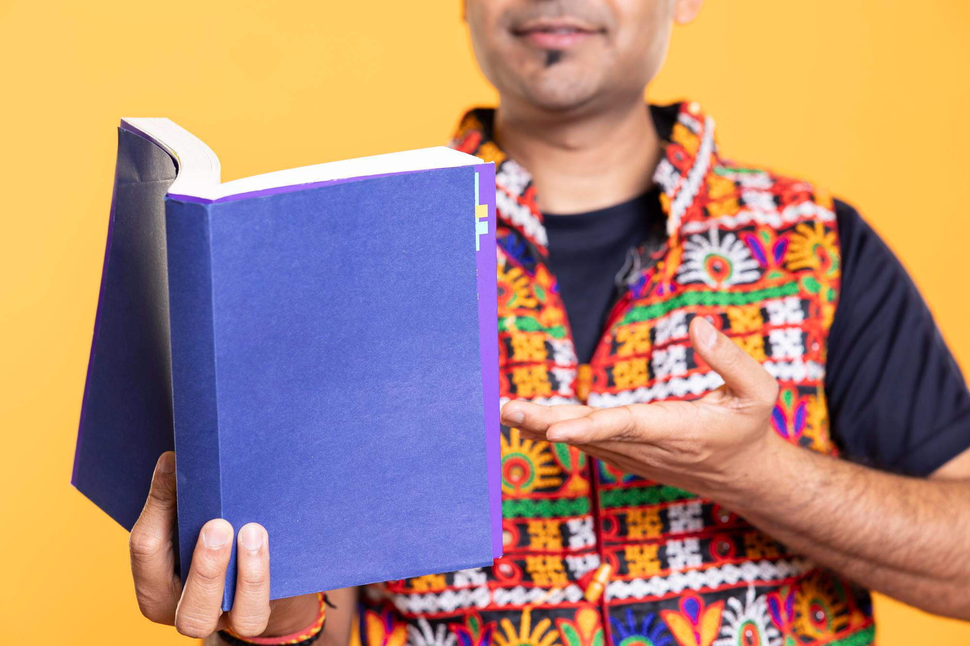 Homem sorridente segurando livro lilás e apontando para ele.