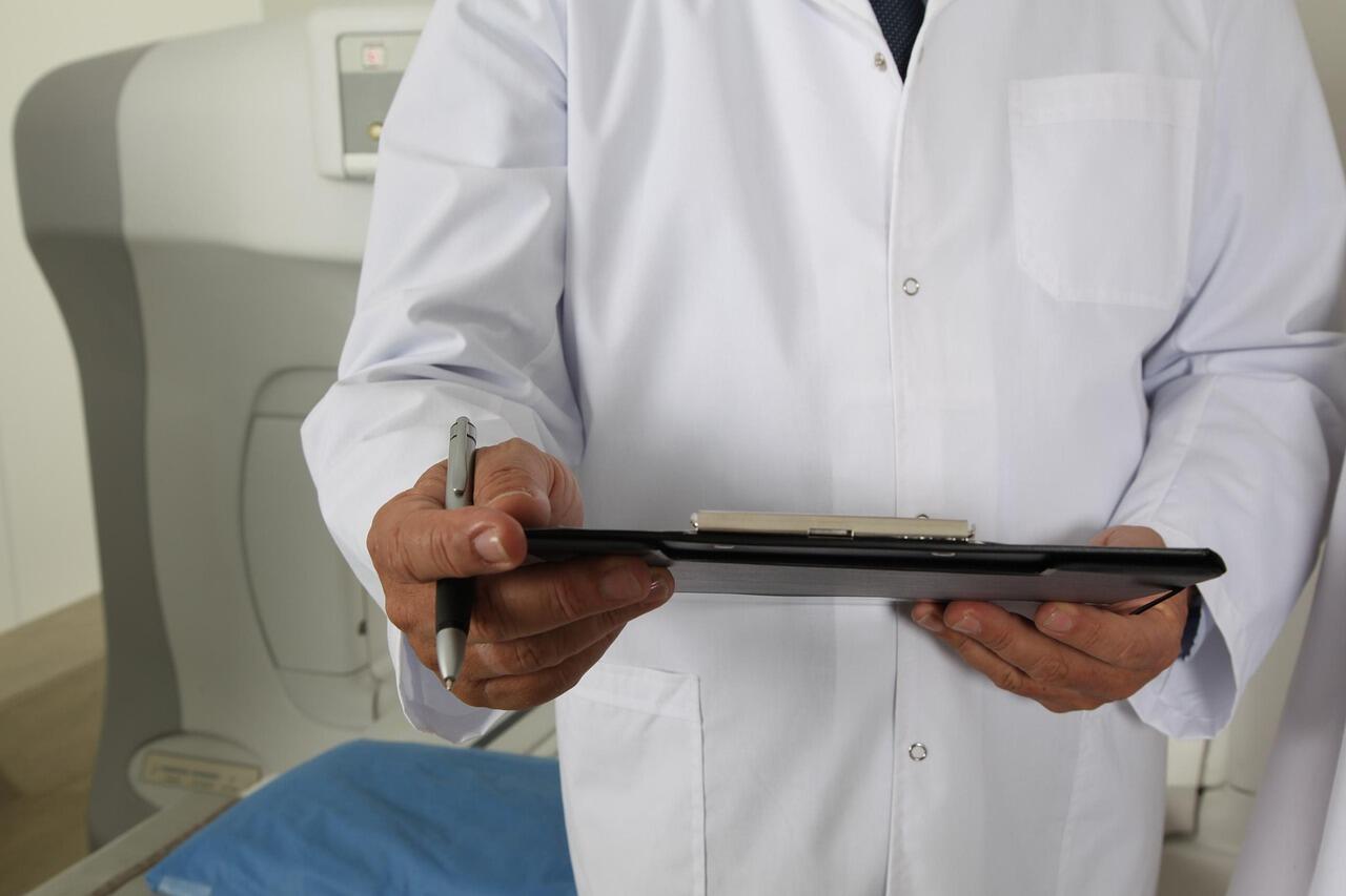 Imagem de um médico de jaleco em frente ao tomógrafo