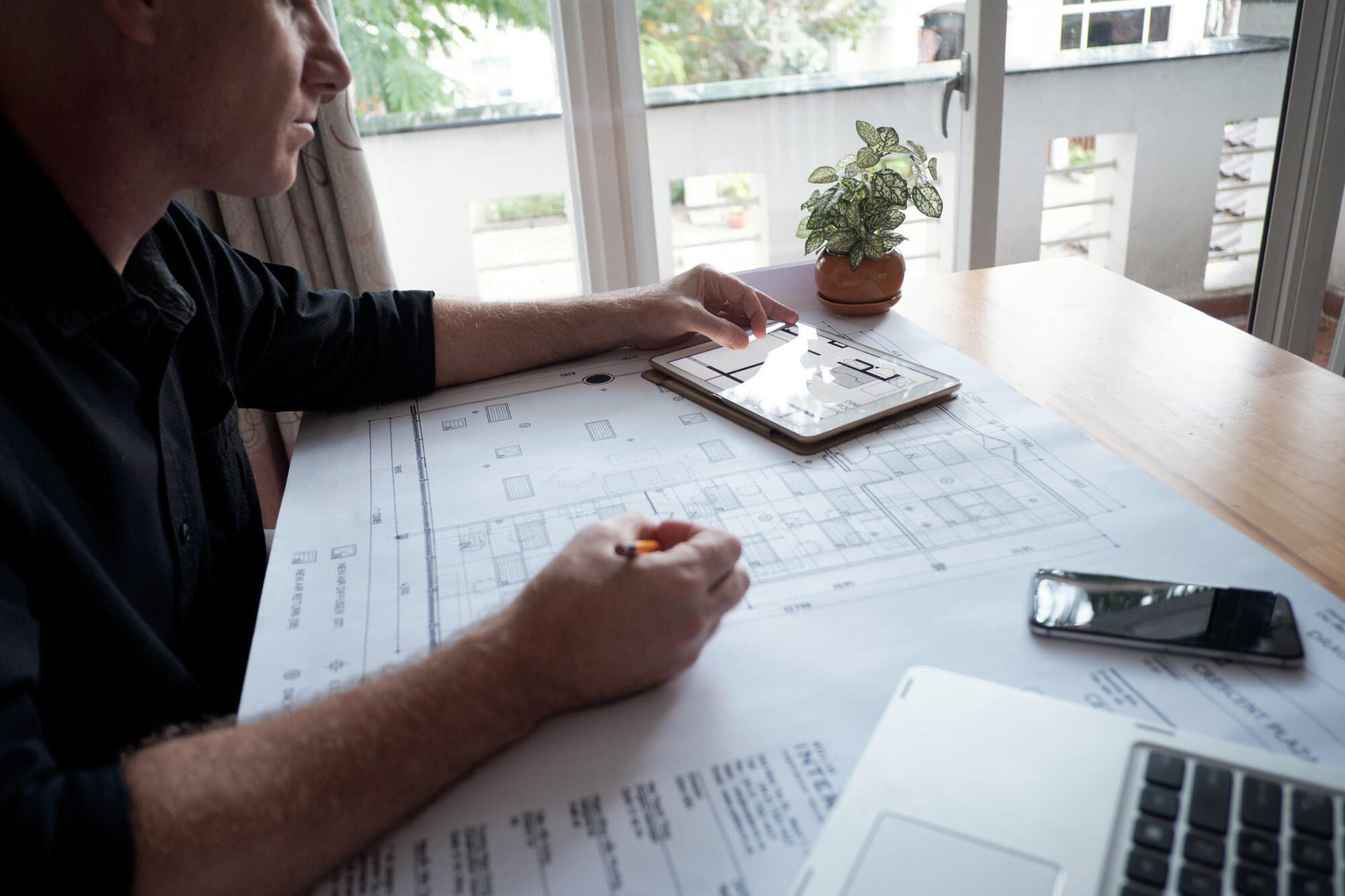 Arquiteto desenhando projeto, com lápis, papel e tablet, em cima da mesa.