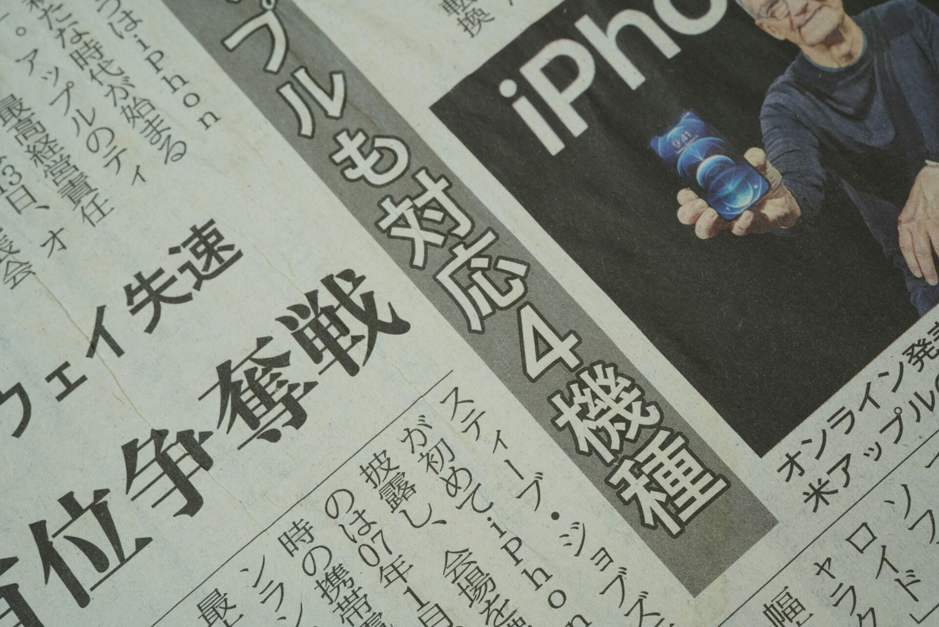 A close-up of a newspaper featuring a headline about the iPhone, with an elderly man holding the device prominently displayed.