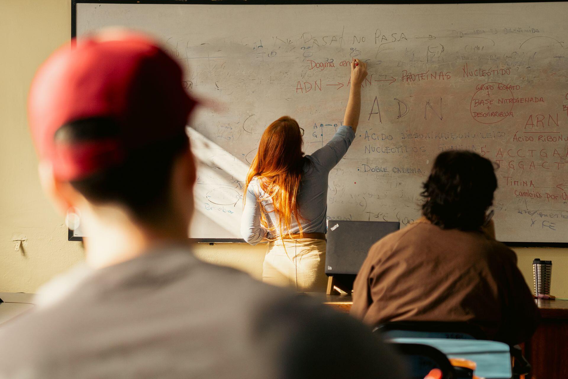 Teacher writing DNA and protein synthesis notes on a whiteboard while students observe in a classroom setting.