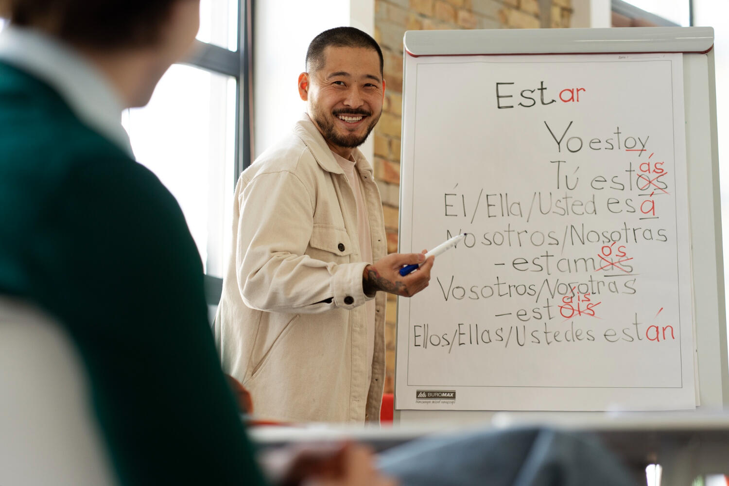 Person teaching Spanish verb conjugation on a whiteboard, pointing at the verb