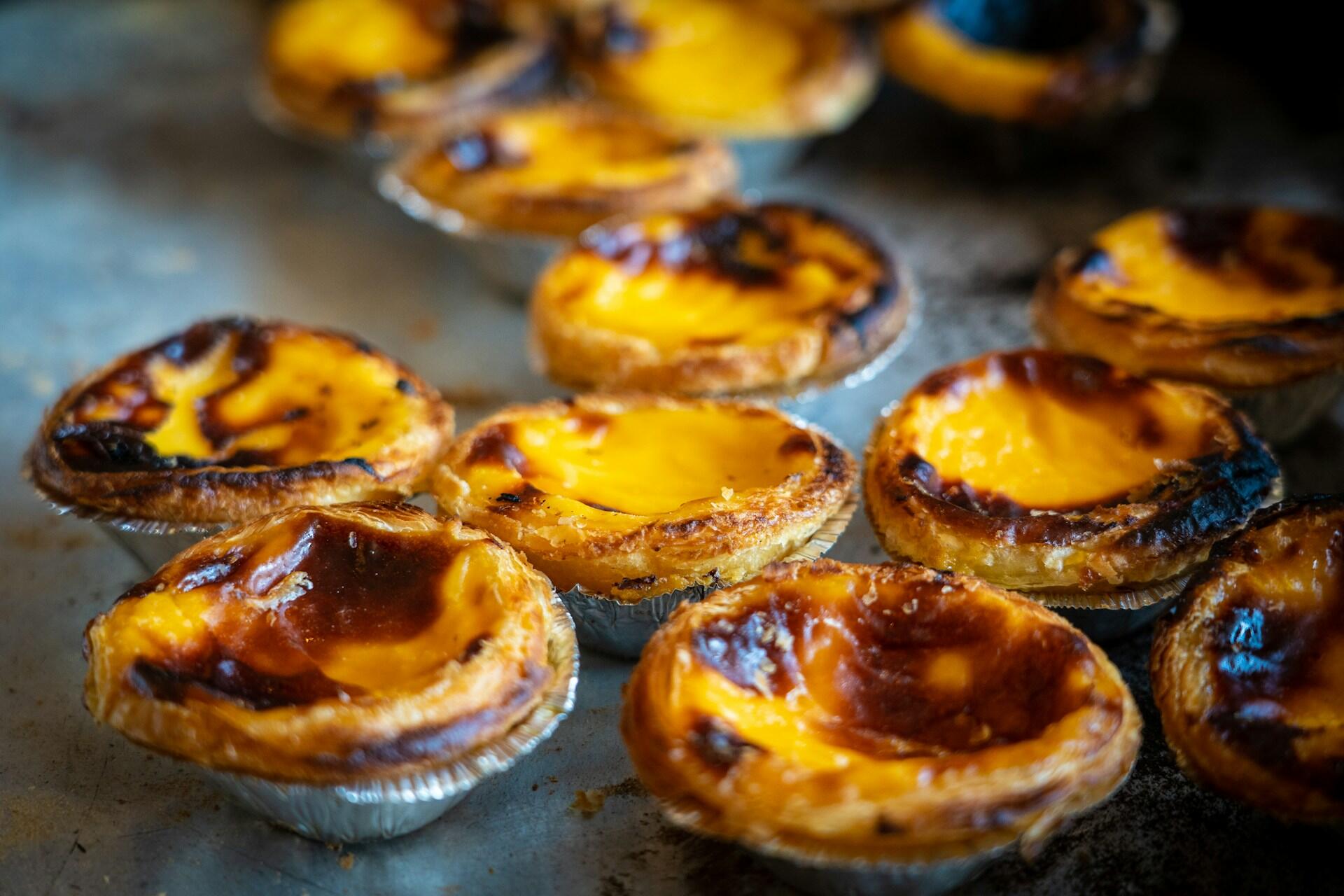 Close-up of several golden-brown pastel de nata custard tarts in foil cups on a baking tray.