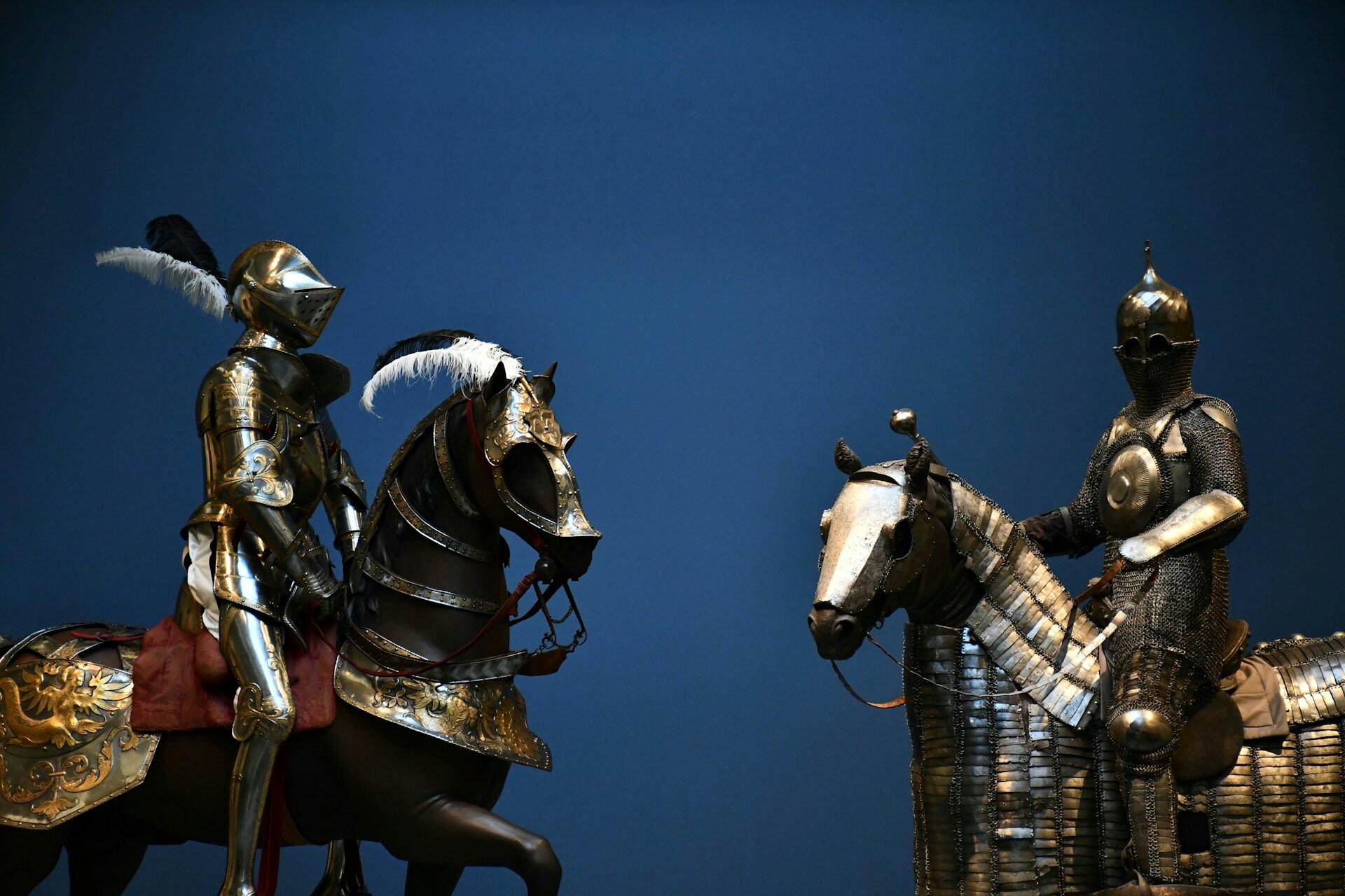 Two medieval knights in ornate armor mounted on armored horses facing each other against a deep blue background.Two medieval knights in ornate armor mounted on armored horses facing each other against a deep blue background.