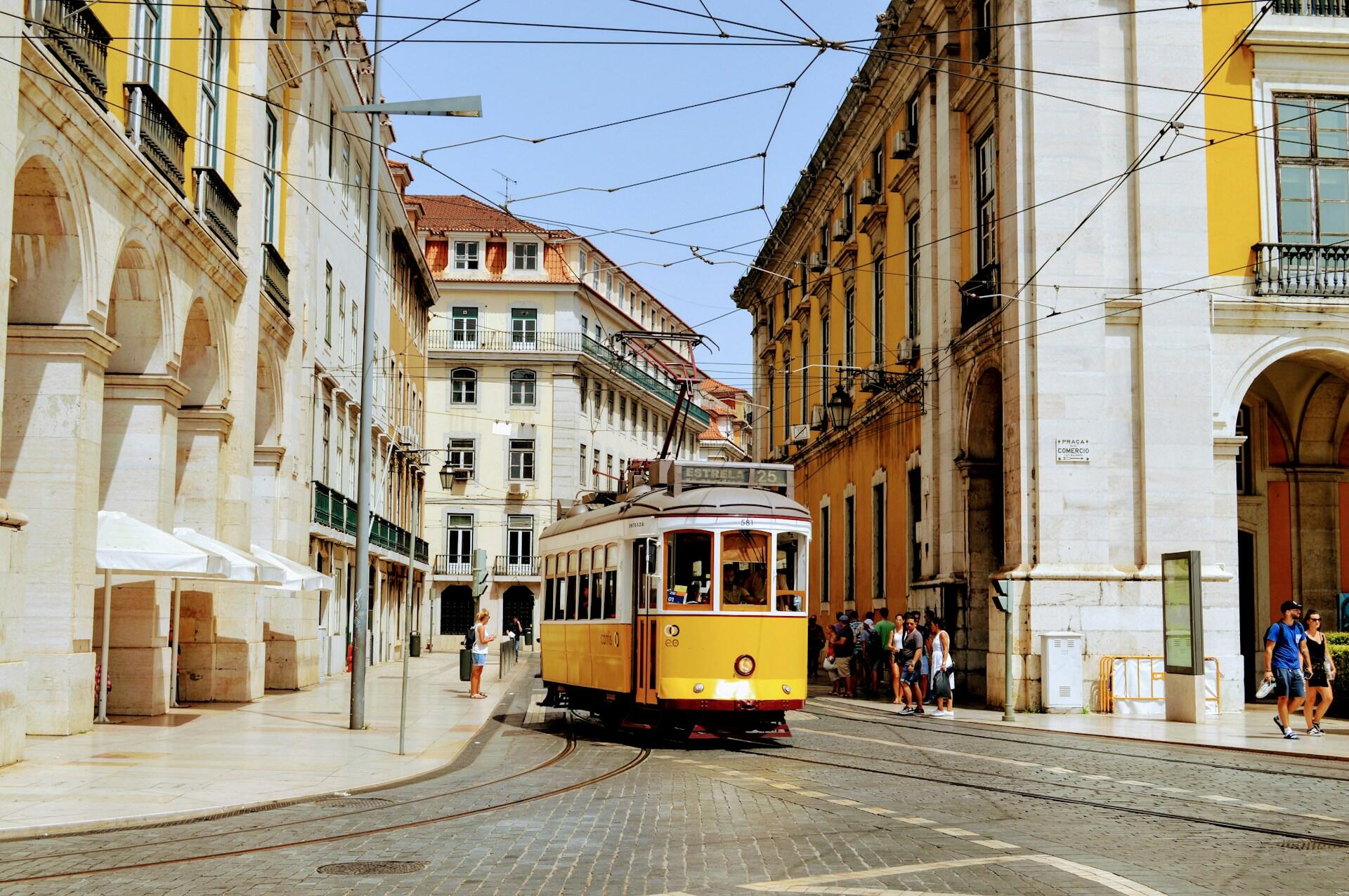 Yellow tram on cobblestone street with historic yellow building and arched windows in sunny urban square.