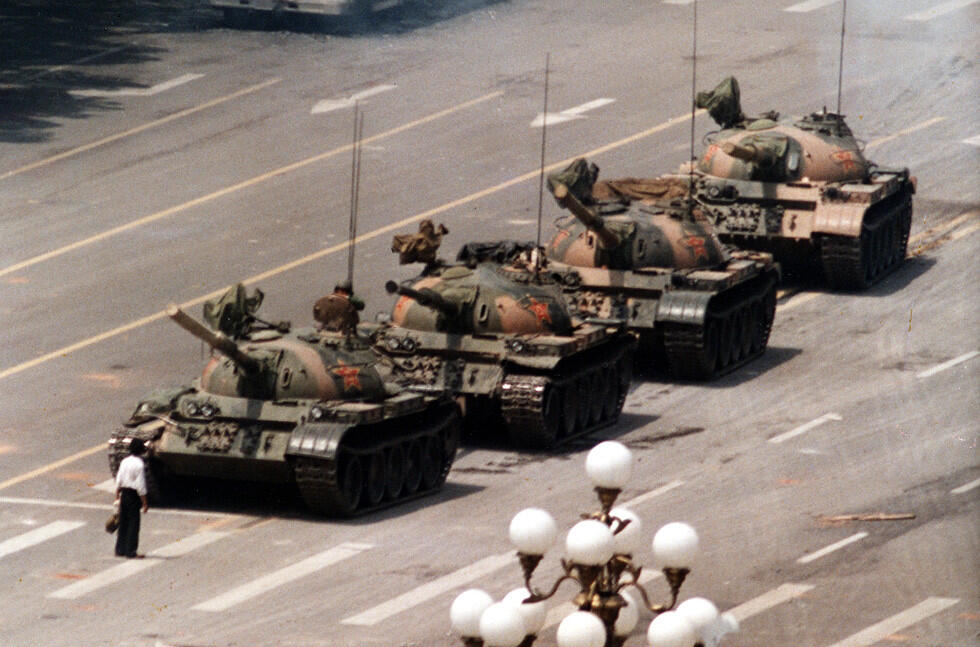 A row of military tanks on a wide urban street, with a lone figure standing in front, signaling defiance and resistance.