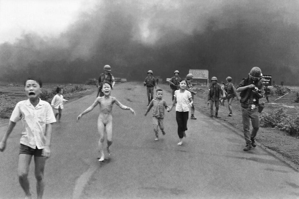 Kids run down the road, one of which is naked, during the Vietnam War, whilst surrounded by soldiers and press.