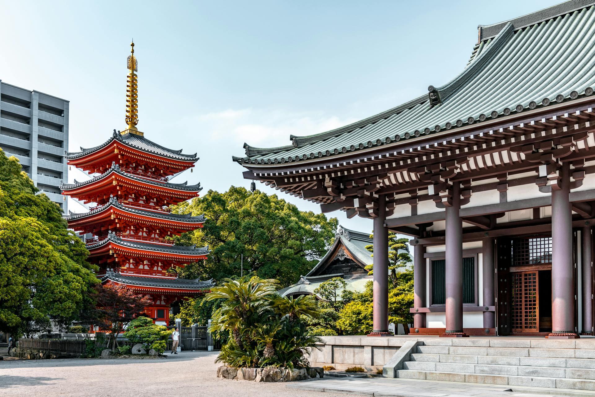 Traditional Japanese temple with a red five-story pagoda surrounded by green trees under a clear sky.