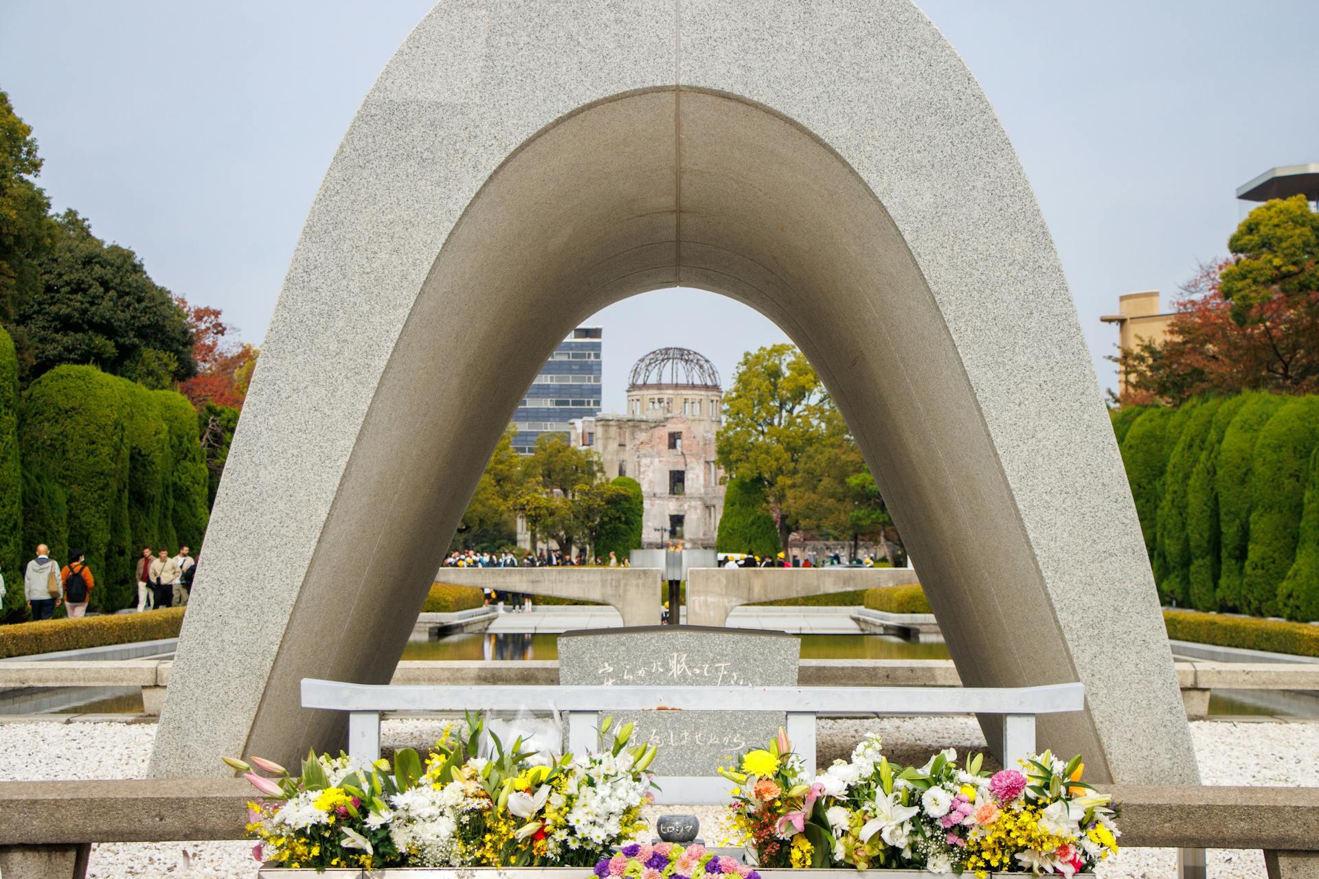 Memorial arch with flowers at Hiroshima Peace Memorial Park, with A-Bomb Dome visible in the background.