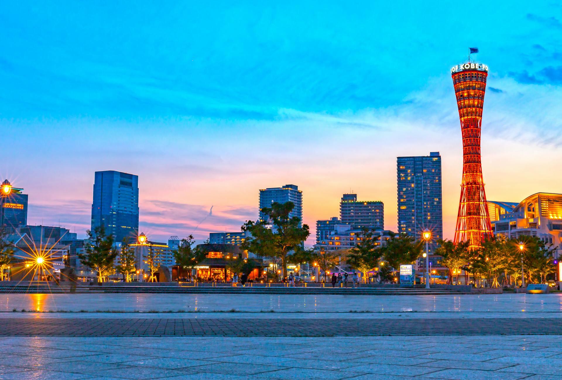 Sunset cityscape with illuminated Kobe Port Tower and surrounding buildings against a blue and orange sky.