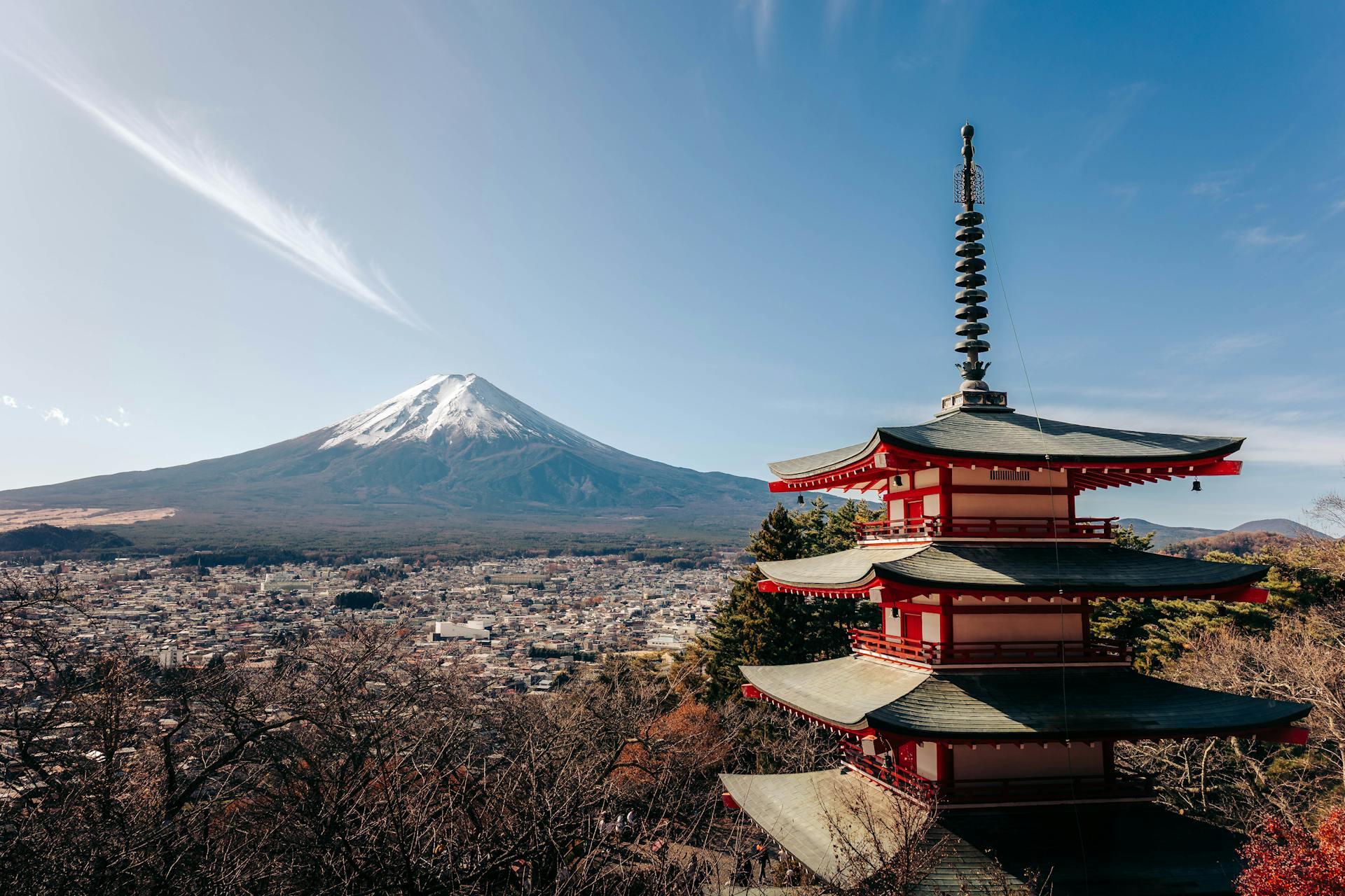 Chureito Pagoda in the foreground with snow-capped Mount Fuji and a cityscape under a clear blue sky.