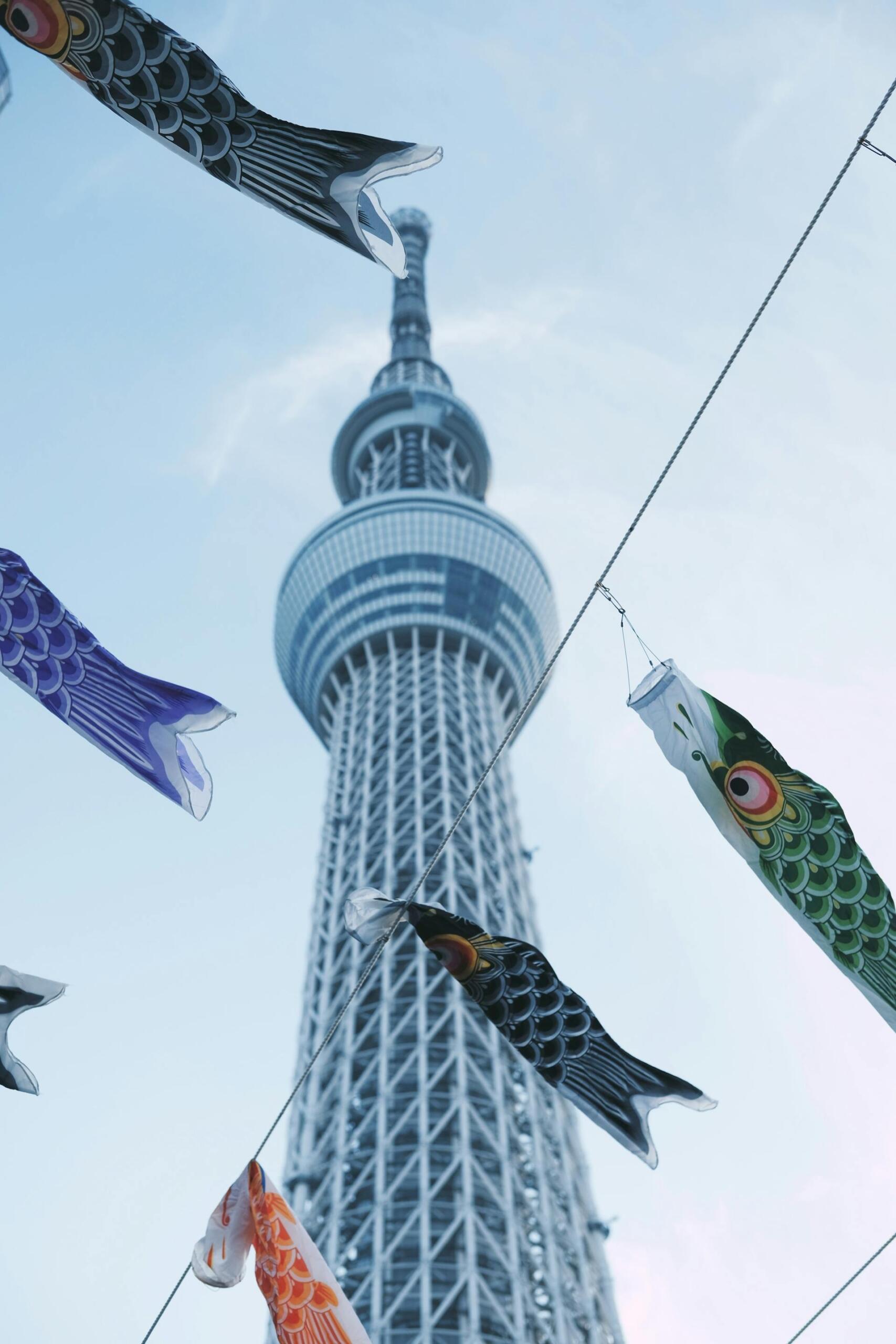 Colorful koi fish-shaped windsocks fluttering against the backdrop of the Tokyo Skytree tower on a clear day.