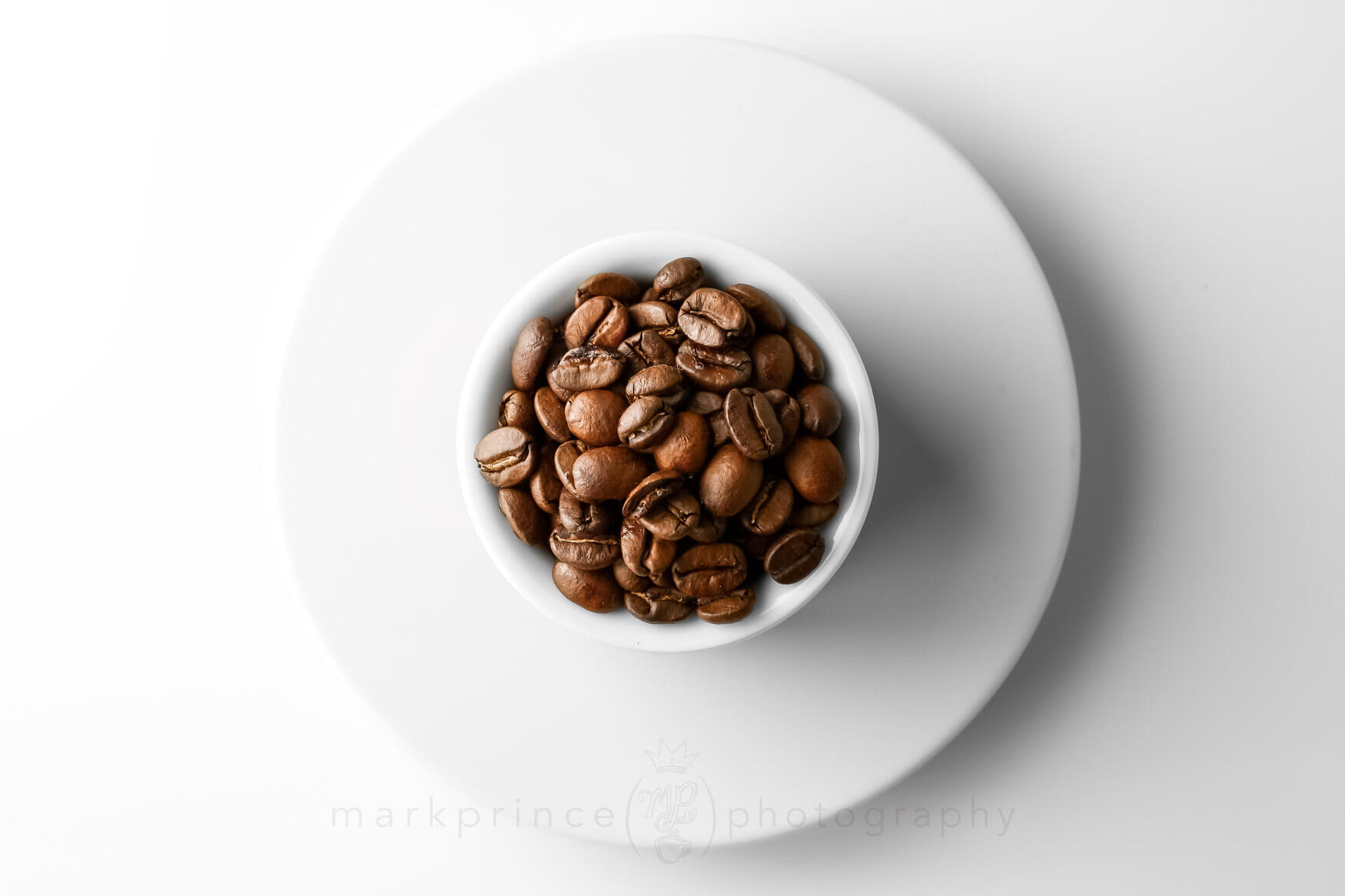 White cup filled with roasted coffee beans placed on a white saucer.